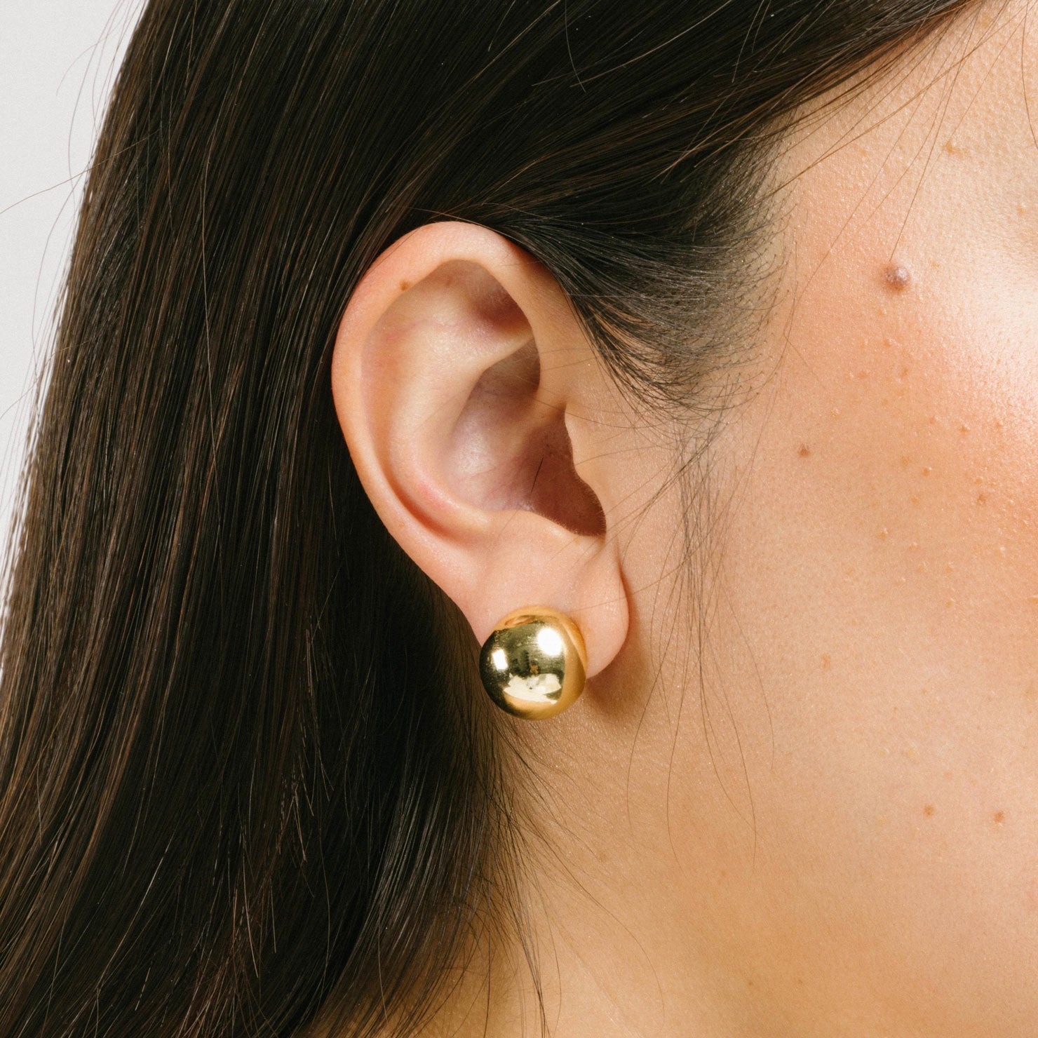 A model wearing the Olive Clip On Earrings feature a Mosquito Coil Clip-On closure type, ideal for all ear types. Average comfortable wear duration is 24 hours, with a medium secure hold. These earrings are adjustable; gently squeeze the padding forward once they are on the ear. Materials are gold tone copper. Please note, item is only one pair.