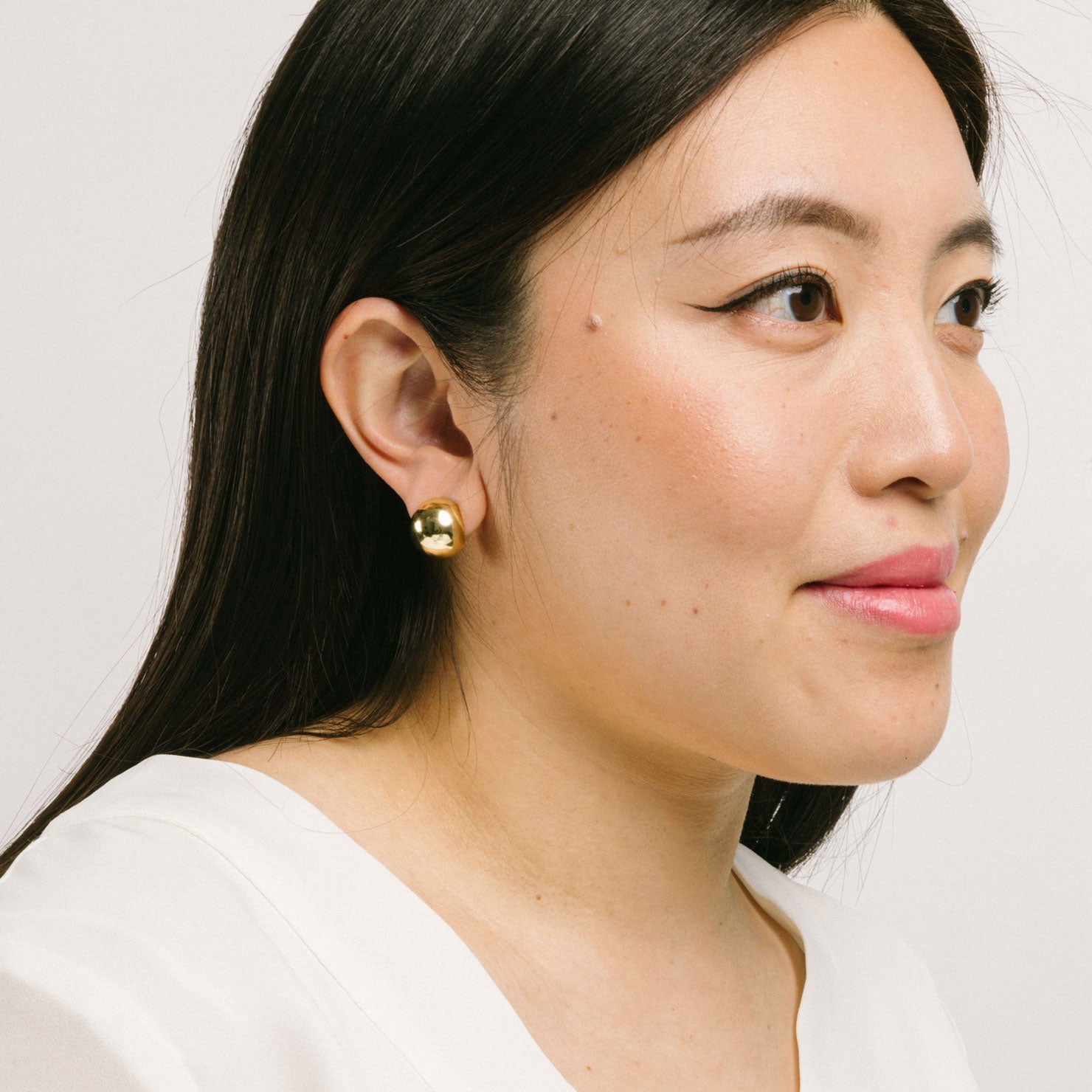 A model wearing the Olive Clip On Earrings feature a Mosquito Coil Clip-On closure type, ideal for all ear types. Average comfortable wear duration is 24 hours, with a medium secure hold. These earrings are adjustable; gently squeeze the padding forward once they are on the ear. Materials are gold tone copper. Please note, item is only one pair.