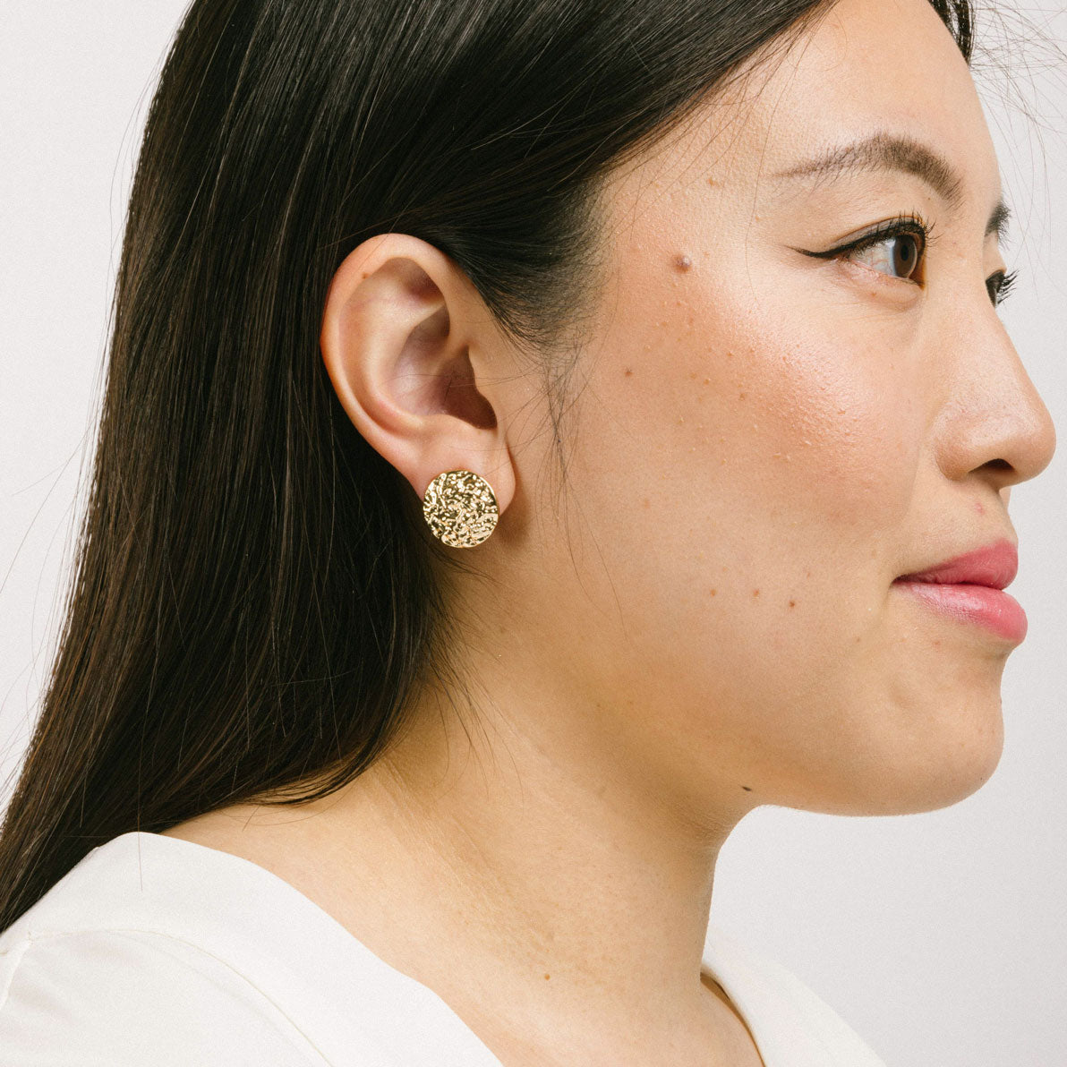 A model wearing the Paloma Clip-On Earrings in Gold provide a secure fit that is perfect for all ear types, including thick/large ears, sensitive ears, small/ thin ears, and stretched/healing ears. These earrings are crafted with a copper alloy and are free of lead and nickel. Their removable rubber padding ensures comfortable wear for up to 12 hours. This package contains one pair of earrings.