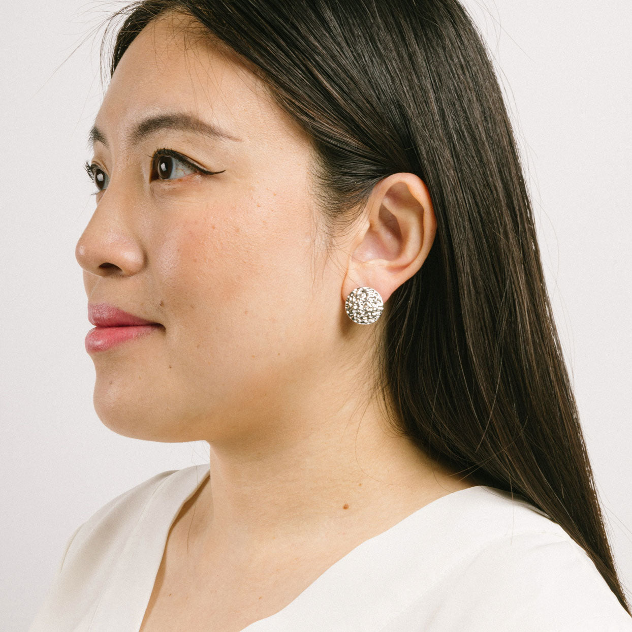 A model wearing the Paloma Clip-On Earrings in Silver provide a secure fit that is perfect for all ear types, including thick/large ears, sensitive ears, small/ thin ears, and stretched/healing ears. These earrings are crafted with a copper alloy and are free of lead and nickel. Their removable rubber padding ensures comfortable wear for up to 12 hours. This package contains one pair of earrings.