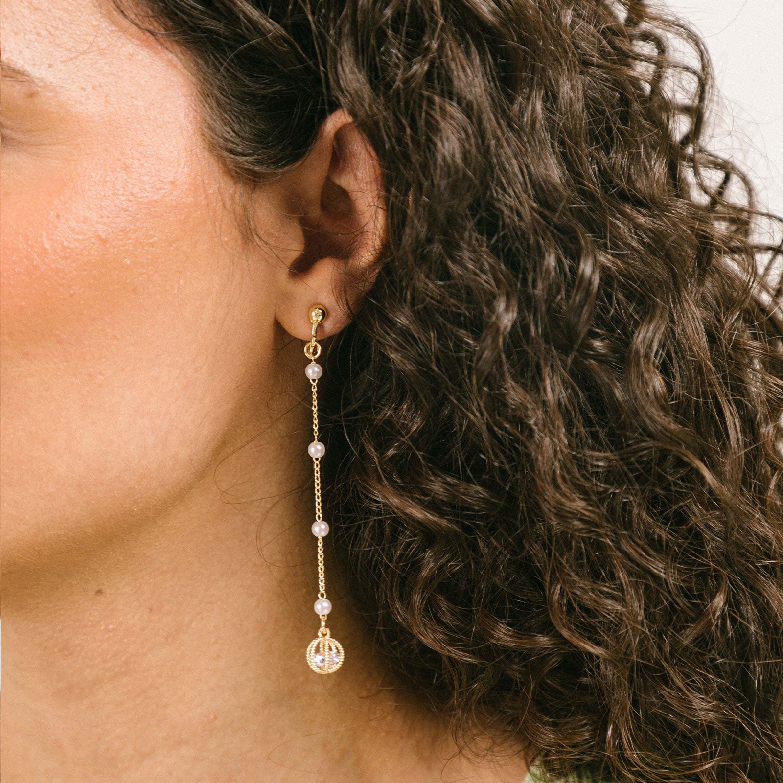 A model wearing the Pearl Drop Clip-On Earrings features a secure screw-back closure. Compatible with all ear types, these earrings provide a comfortable wear of 8-12 hours and offer an adjustable hold strength. Constructed with gold-tone plated metal alloy and a faux pearl, this single pair of earrings is sure to become a favorite.