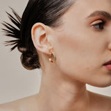 A model wearing the Pleated Hoop Clip On Earrings in Gold offer a resin clip-on closure for a secure and comfortable fit for a variety of ear sizes and sensitivities. With an average wear duration of 8-12 hours, these earrings are perfect for all-day wear. Please note that this listing is for a single pair