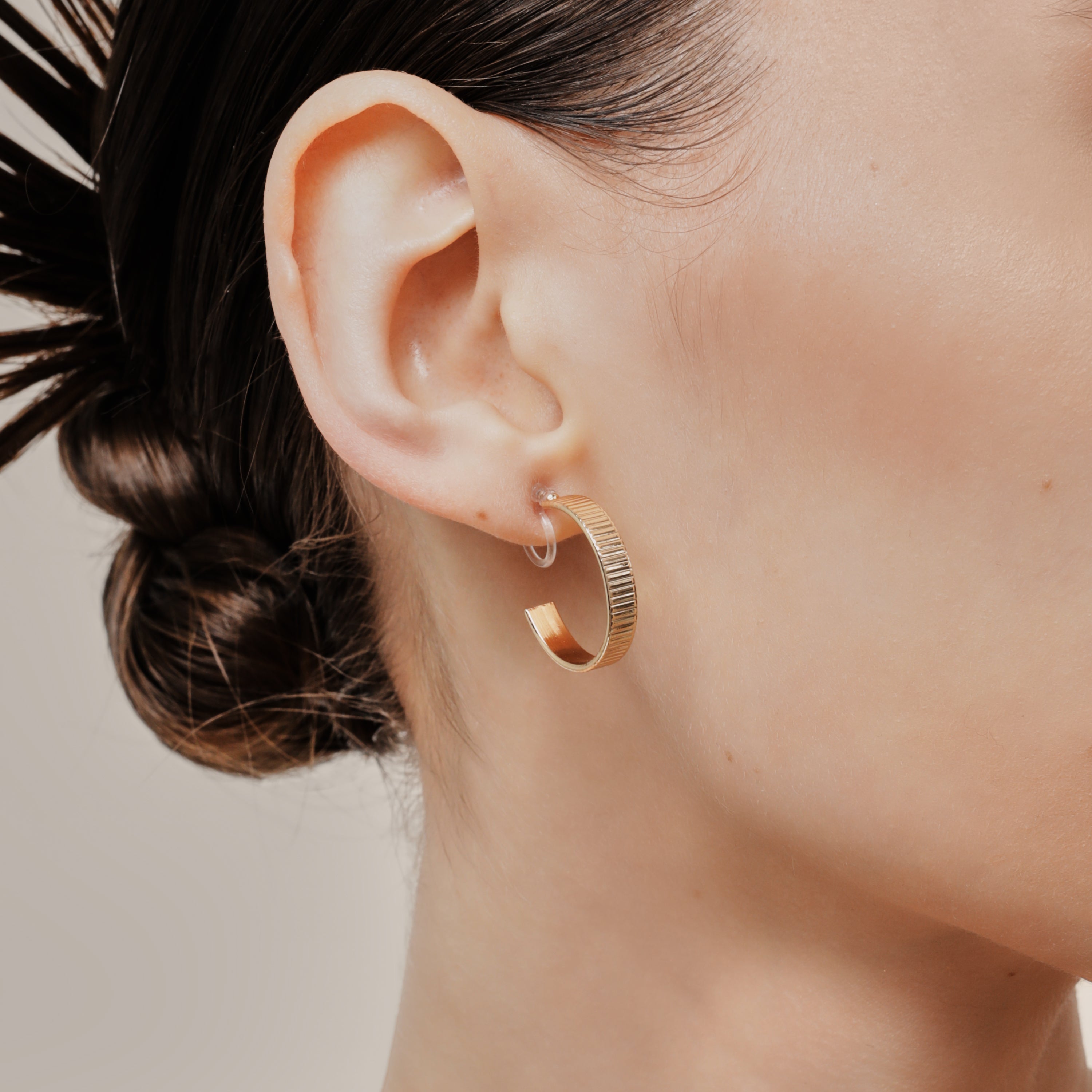 A model wearing the Pleated Hoop Clip On Earrings in Gold offer a resin clip-on closure for a secure and comfortable fit for a variety of ear sizes and sensitivities. With an average wear duration of 8-12 hours, these earrings are perfect for all-day wear. Please note that this listing is for a single pair