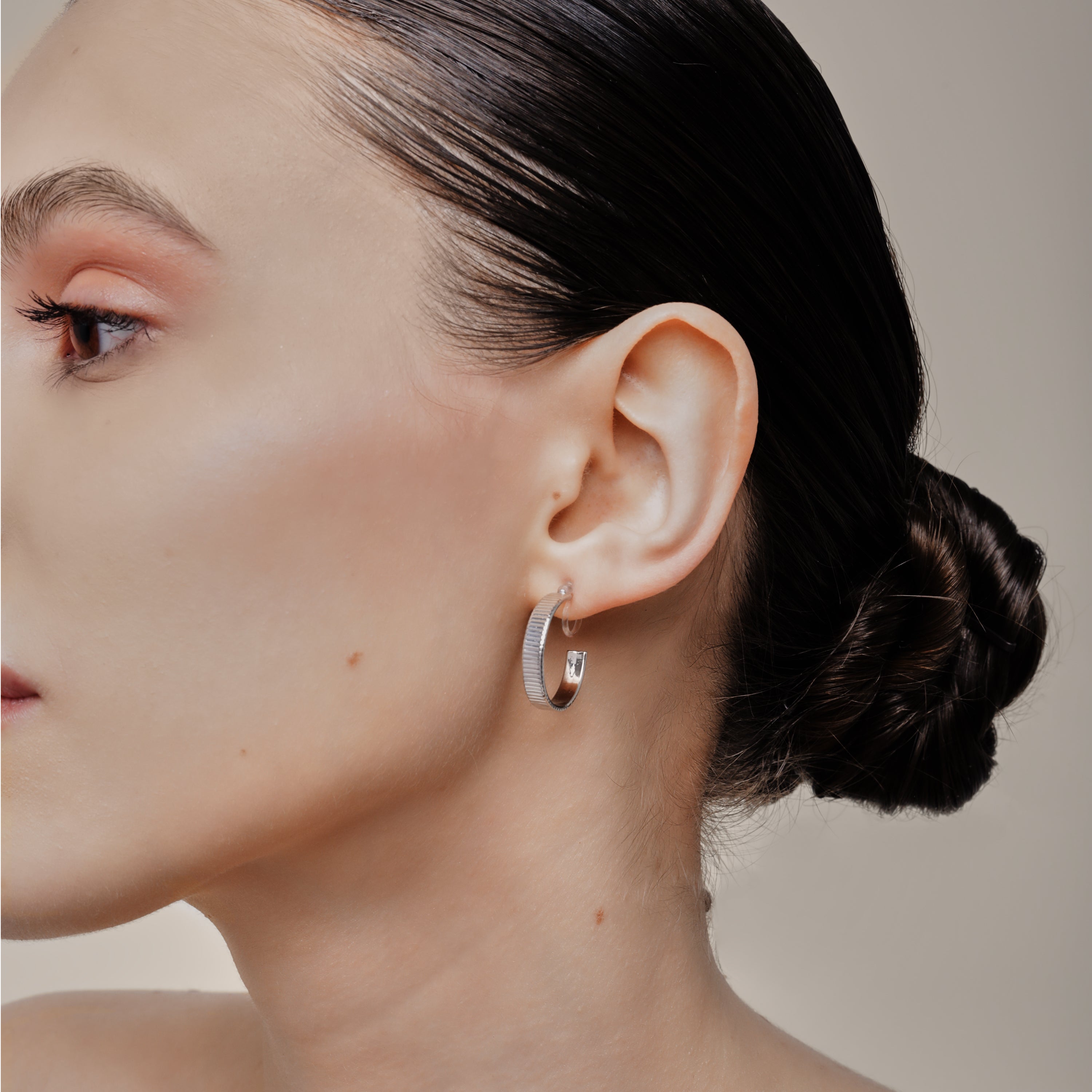 A model wearing the Pleated Hoop Clip On Earrings in Silver offer a resin clip-on closure for a secure and comfortable fit for a variety of ear sizes and sensitivities. With an average wear duration of 8-12 hours, these earrings are perfect for all-day wear. Please note that this listing is for a single pair