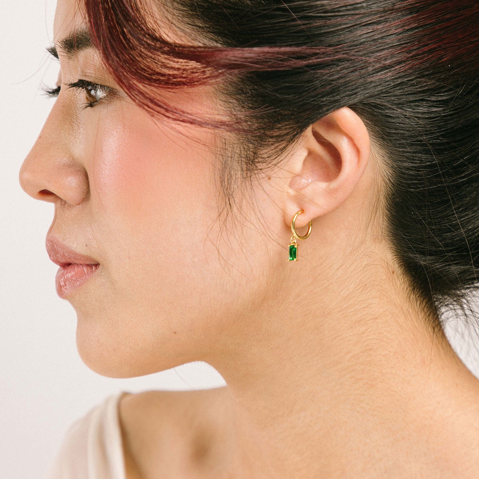 A model wearing the Rectangle Gem Clip-On Earrings offer a reliable, secure fit, thanks to their sliding spring closure. Suited for smaller or thinner earlobes, these earrings will typically remain comfortable for 2-4 hours. With an adjustable design, they will automatically adjust to your ear thickness. Each pair is crafted from brass and cubic zirconia.