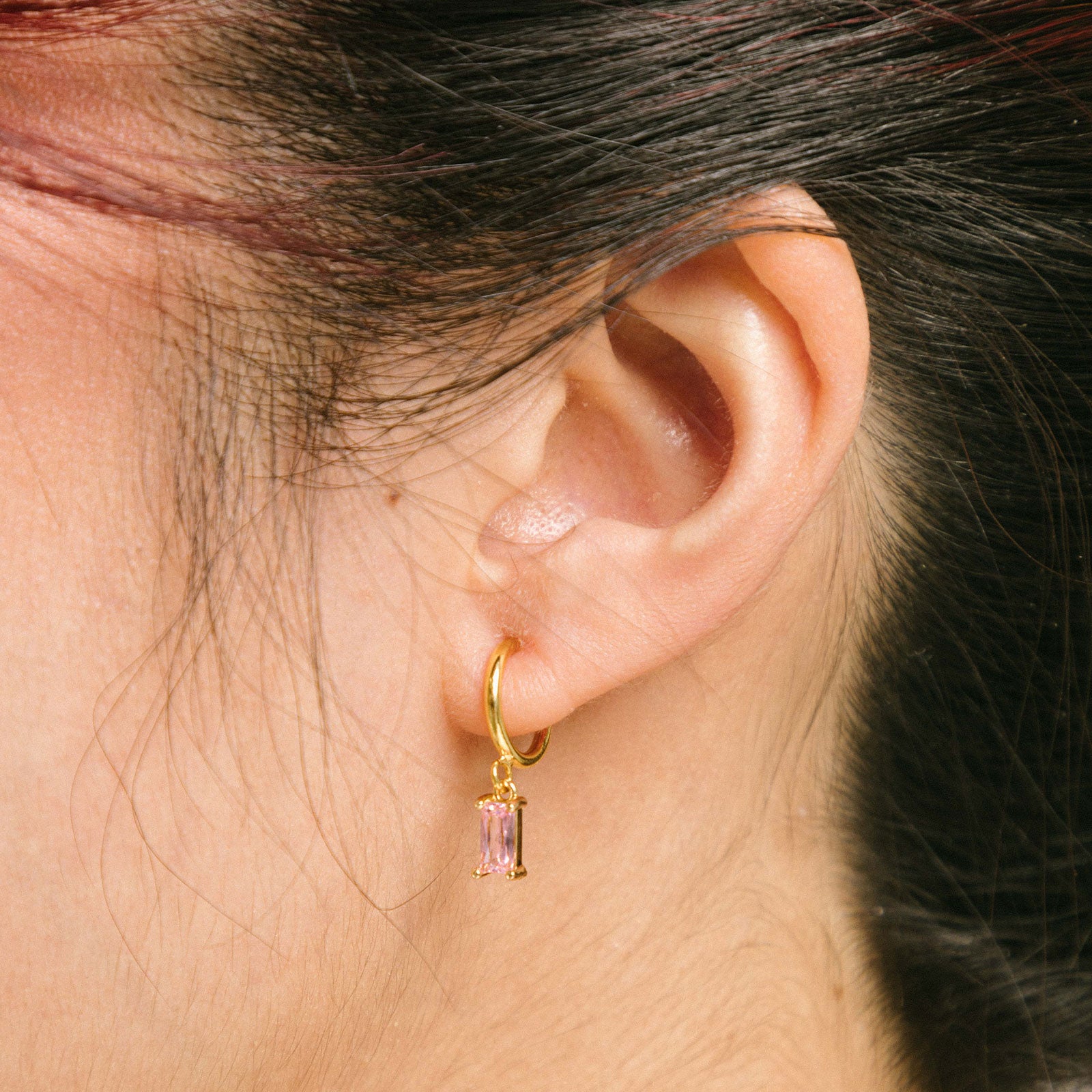 A model wearing the Rectangle Gem Clip-On Earrings offer a reliable, secure fit, thanks to their sliding spring closure. Suited for smaller or thinner earlobes, these earrings will typically remain comfortable for 2-4 hours. With an adjustable design, they will automatically adjust to your ear thickness. Each pair is crafted from brass and cubic zirconia.