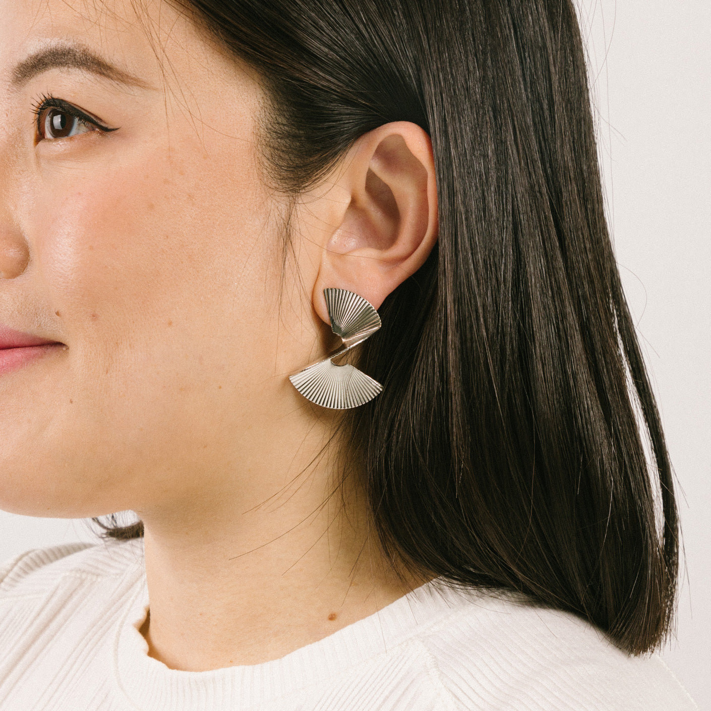 A model wearing the Ribbed Swirl Clip On Earrings in Silver feature a padded clip-on closure that can be worn comfortably for 8-12 hours. Made with silver tone copper alloy, these earrings provide a secure hold that can be adjusted to fit all ear types, such as thick/large, sensitive, small/thin, and stretched/healing. Please note, item is sold as one pair.