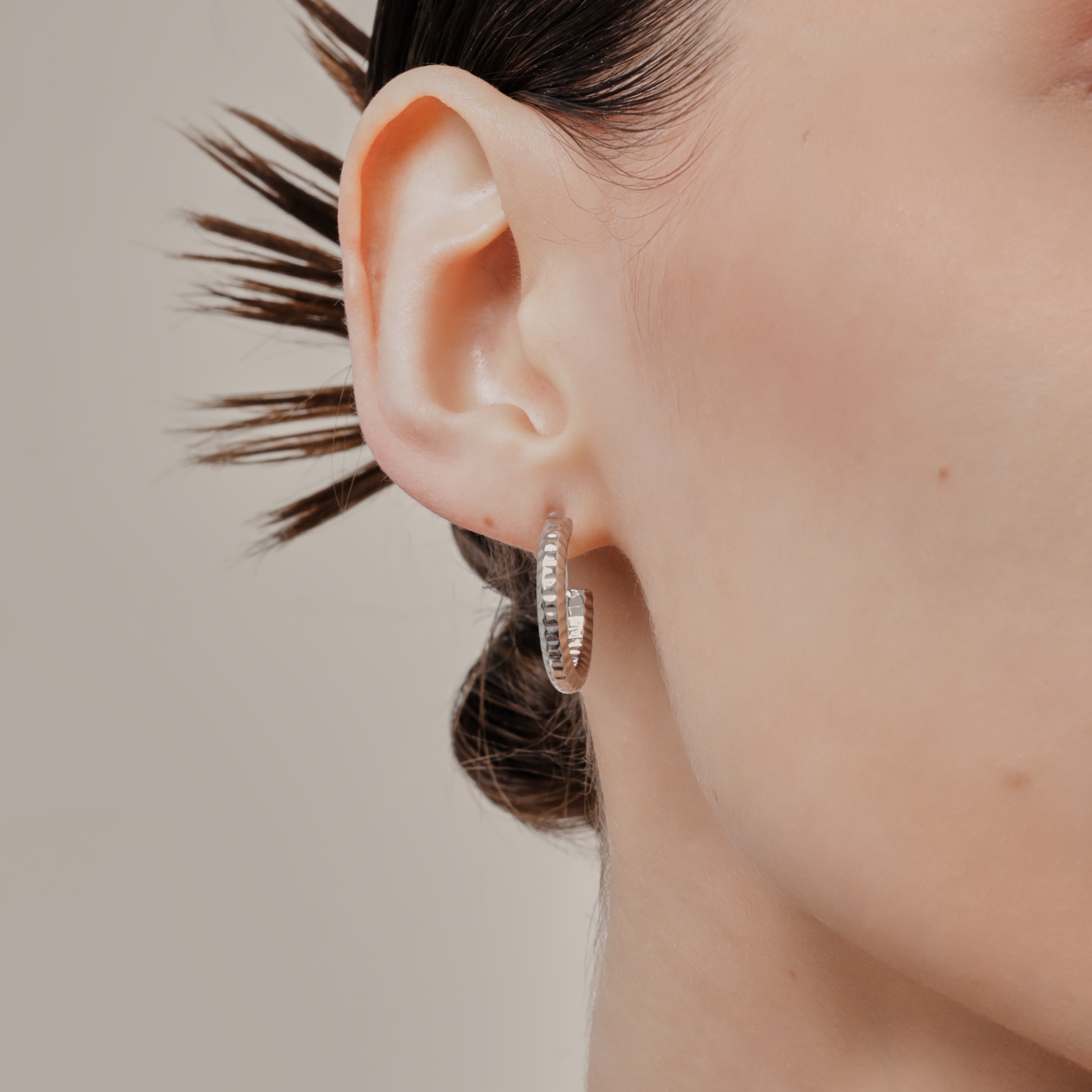 A model wearing the Ribbed Hoop Clip On Earrings in Silver. Made with a Resin Clip-On closure, these earrings provide a secure hold for 8-12 hours and are suitable for all ear sizes and types. Elevate your look with these versatile and long-lasting earrings. Set includes one pair.