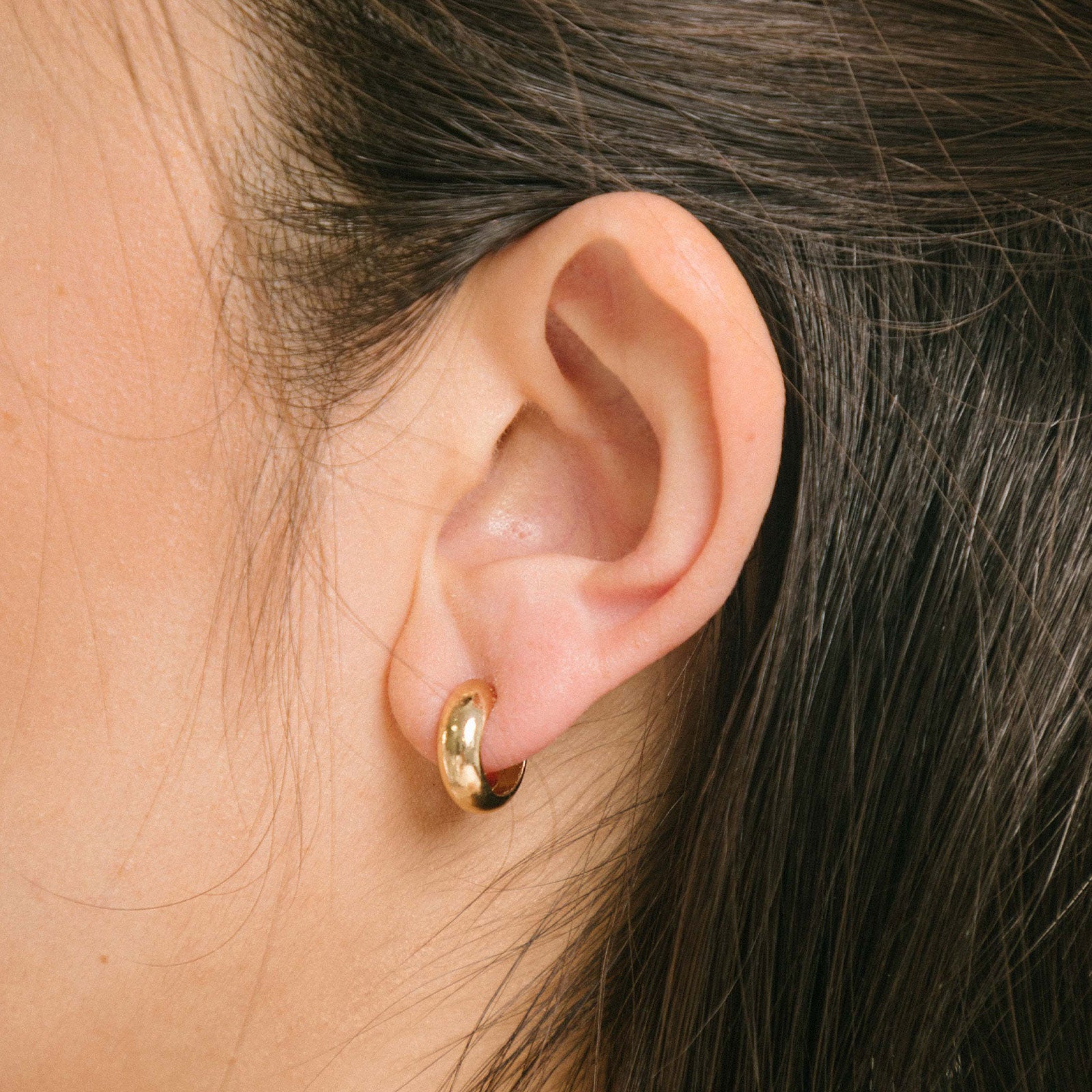 Model wearing the Simple Gold  Huggie Clip-On Earrings provide a medium secure hold, making them perfect for all ear types. With adjustable padding for extra comfort, these earrings can be worn for up to 24 hours with ease.