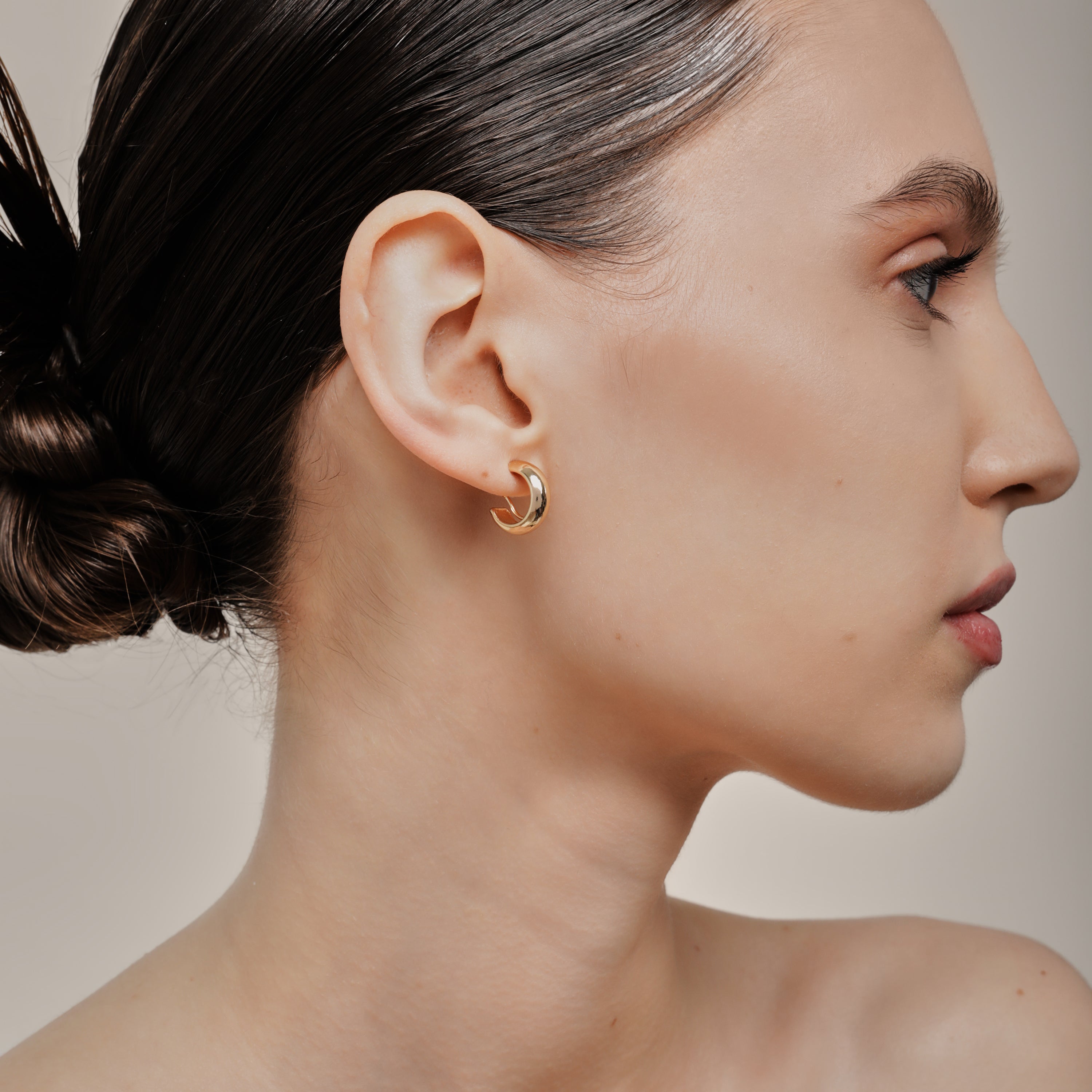 A model wearing the Simple Gold Huggie Clip-On Earrings feature a mosquito coil closure ideal for all ear types, providing a medium-secure hold and comfortable wear for up to 24 hours. These earrings can be adjusted with a gentle squeeze of the padding forward once on the ear. Crafted with Gold tone plated copper alloy, these sophisticated earrings are also available in Silver.
