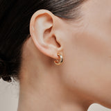 A model wearing the Simple Gold Huggie Clip-On Earrings feature a mosquito coil closure ideal for all ear types, providing a medium-secure hold and comfortable wear for up to 24 hours. These earrings can be adjusted with a gentle squeeze of the padding forward once on the ear. Crafted with Gold tone plated copper alloy, these sophisticated earrings are also available in Silver.