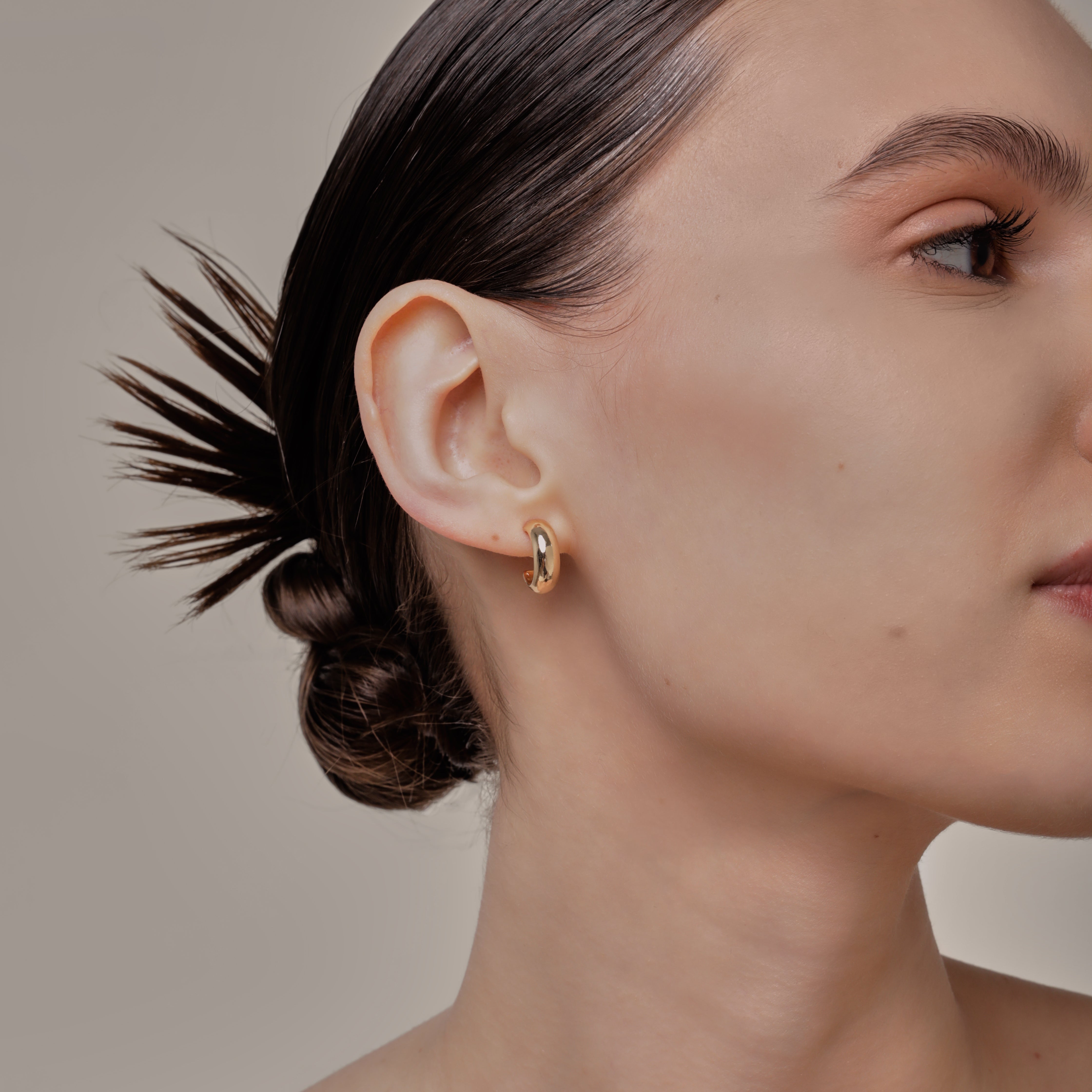 A model wearing the Simple Gold Huggie Clip-On Earrings feature a mosquito coil closure ideal for all ear types, providing a medium-secure hold and comfortable wear for up to 24 hours. These earrings can be adjusted with a gentle squeeze of the padding forward once on the ear. Crafted with Gold tone plated copper alloy, these sophisticated earrings are also available in Silver.