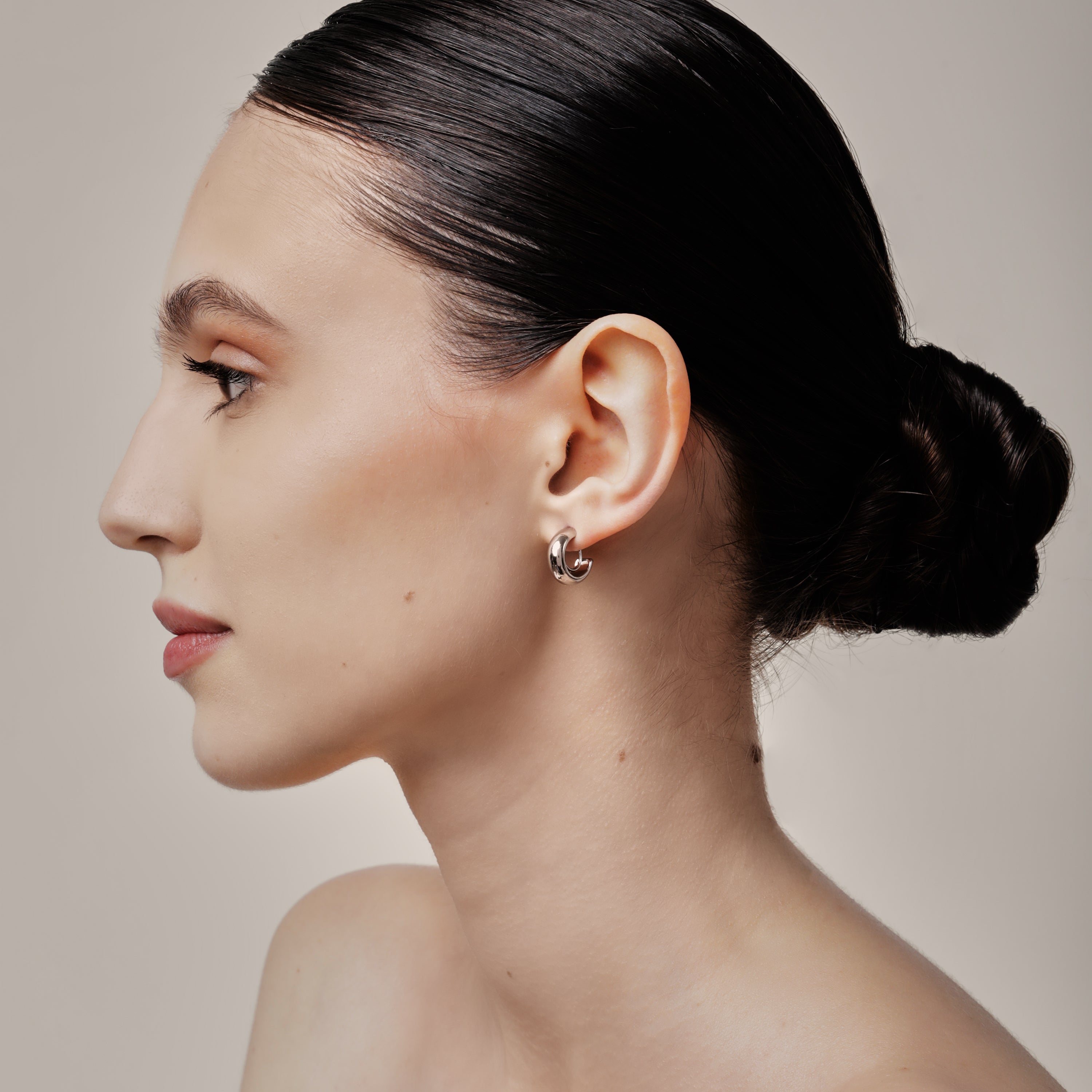 A model wearing the Simple Silver Huggie Clip-On Earrings provide a medium secure hold, making them perfect for all ear types. With adjustable padding for extra comfort, these earrings can be worn for up to 24 hours with ease. Crafted from copper alloy, they are also available in a gold finish.