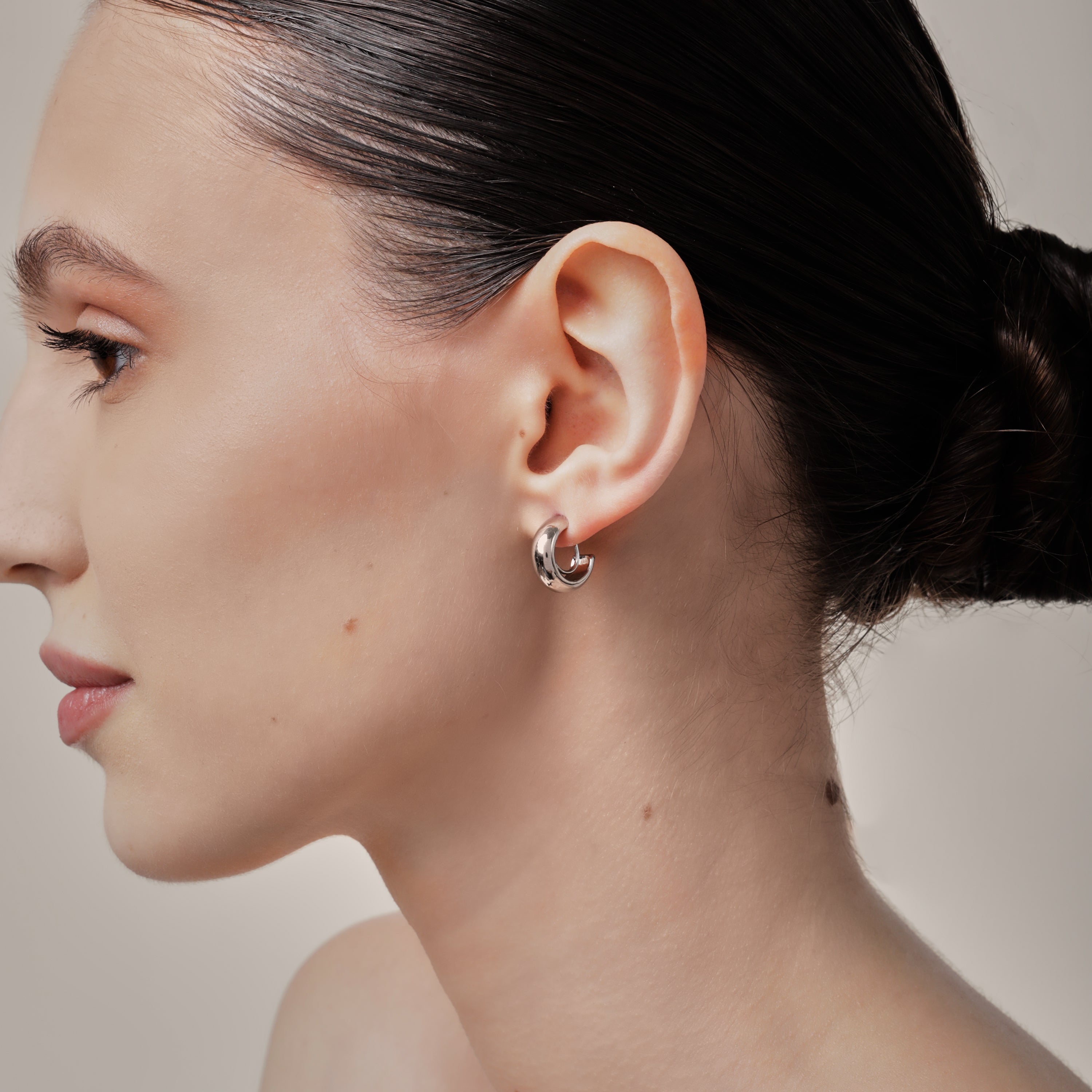 A model wearing the Simple Silver Huggie Clip-On Earrings provide a medium secure hold, making them perfect for all ear types. With adjustable padding for extra comfort, these earrings can be worn for up to 24 hours with ease. Crafted from copper alloy, they are also available in a gold finish.