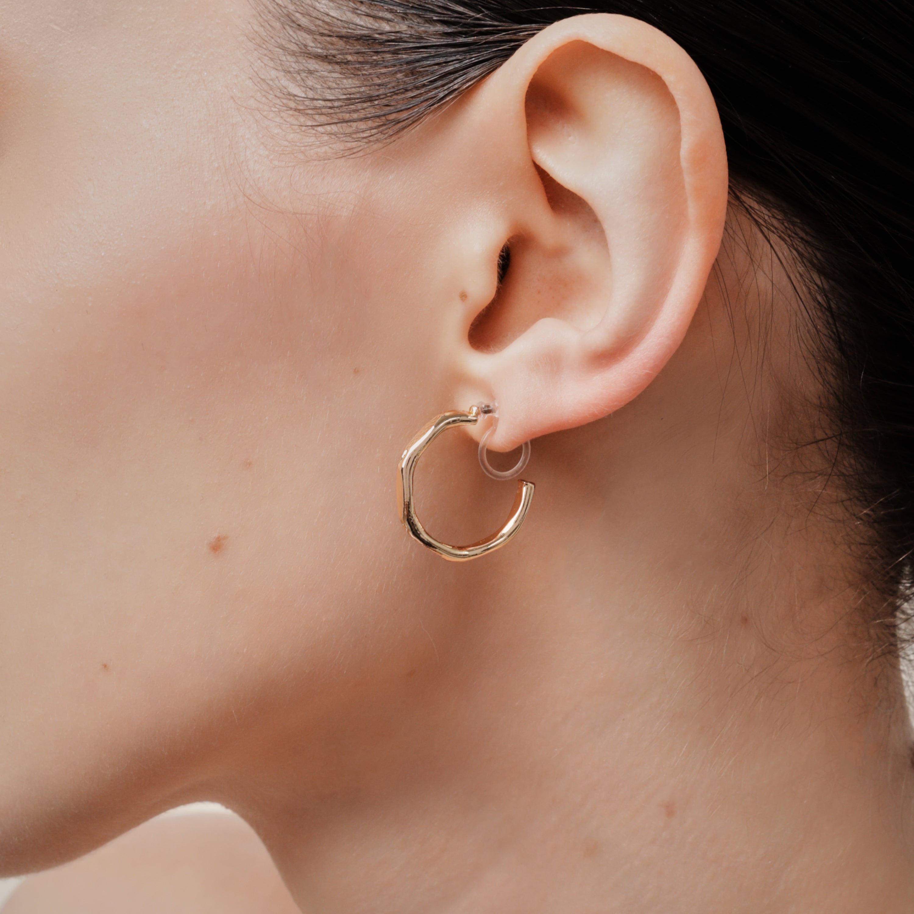 A model wearing the Smith Hoop Clip On Earrings in Gold, perfect for all ear sizes. With a resin clip-on closure and medium secure hold, these earrings provide comfort for 8-12 hours. Whether you have thick, large, or sensitive ears, these earrings are a must-have! Note: No adjustments possible and one pair only.
