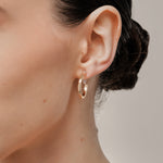 A model wearing the Smith Hoop Clip On Earrings in Gold, perfect for all ear sizes. With a resin clip-on closure and medium secure hold, these earrings provide comfort for 8-12 hours. Whether you have thick, large, or sensitive ears, these earrings are a must-have! Note: No adjustments possible and one pair only.