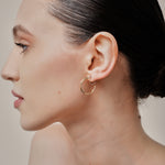 A model wearing the Smith Hoop Clip On Earrings in Gold, perfect for all ear sizes. With a resin clip-on closure and medium secure hold, these earrings provide comfort for 8-12 hours. Whether you have thick, large, or sensitive ears, these earrings are a must-have! Note: No adjustments possible and one pair only.