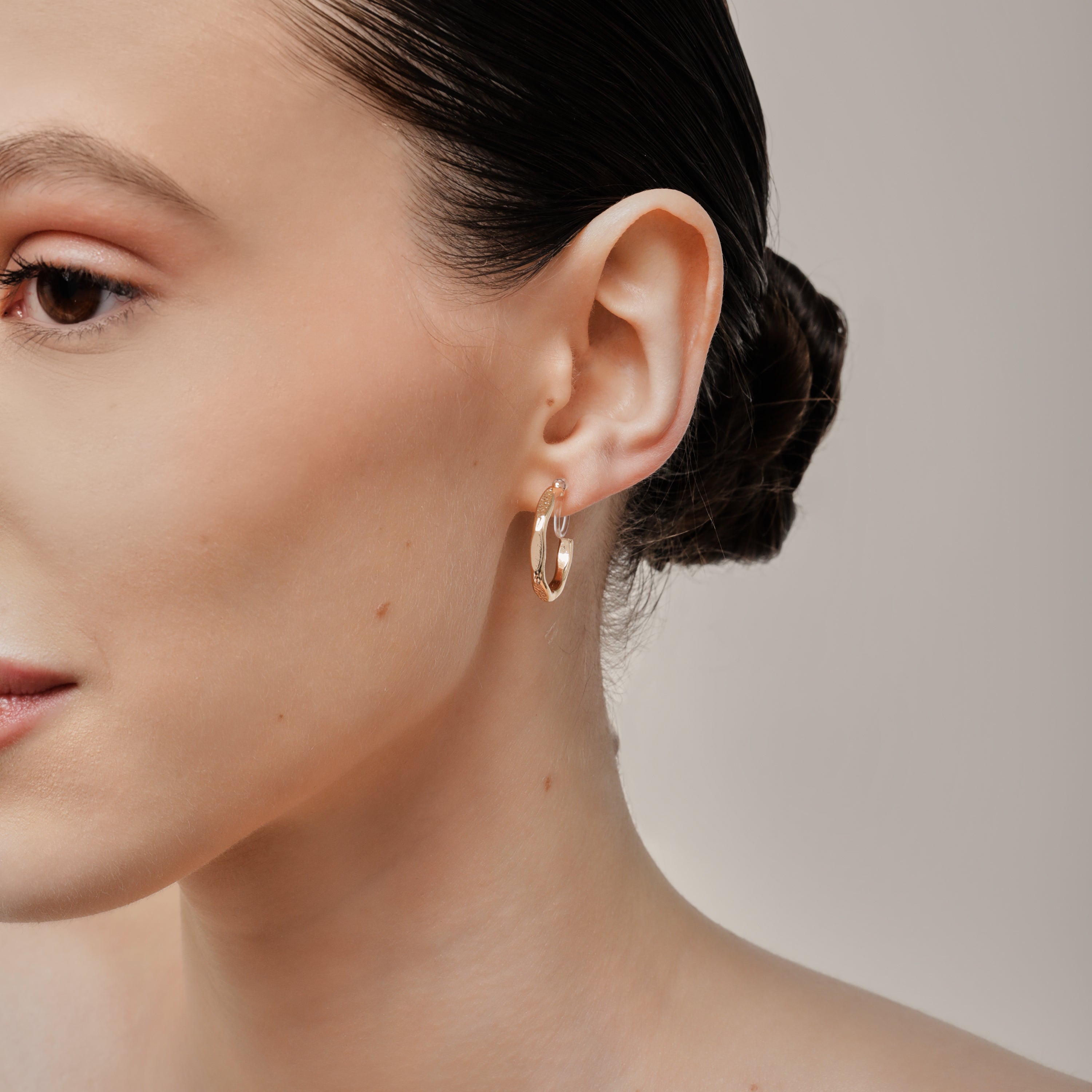 A model wearing the Smith Hoop Clip On Earrings in Gold, perfect for all ear sizes. With a resin clip-on closure and medium secure hold, these earrings provide comfort for 8-12 hours. Whether you have thick, large, or sensitive ears, these earrings are a must-have! Note: No adjustments possible and one pair only.