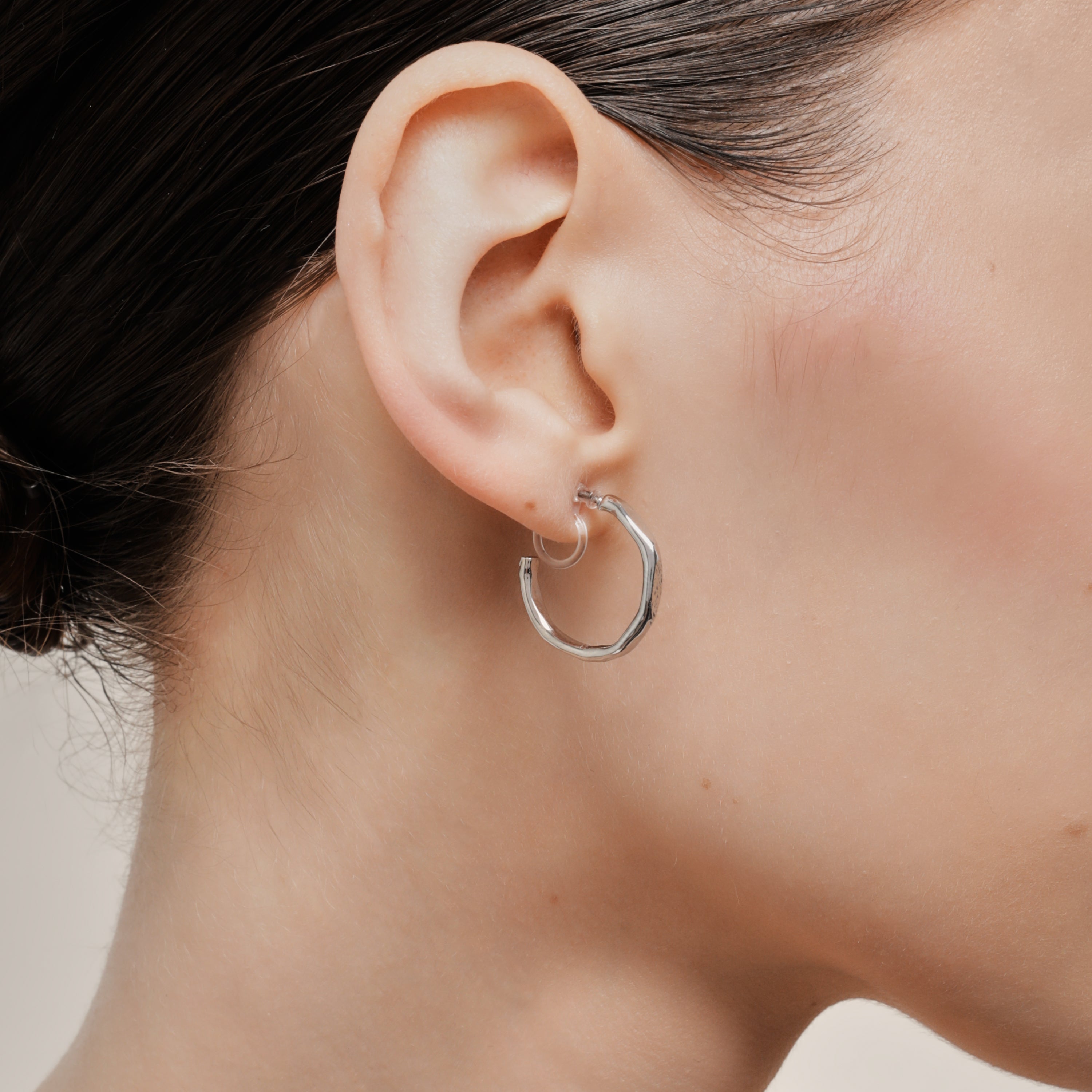 A model wearing the Smith Hoop Clip On Earrings in Silver, perfect for all ear sizes. With a resin clip-on closure and medium secure hold, these earrings provide comfort for 8-12 hours. Whether you have thick, large, or sensitive ears, these earrings are a must-have! Note: No adjustments possible and one pair only.