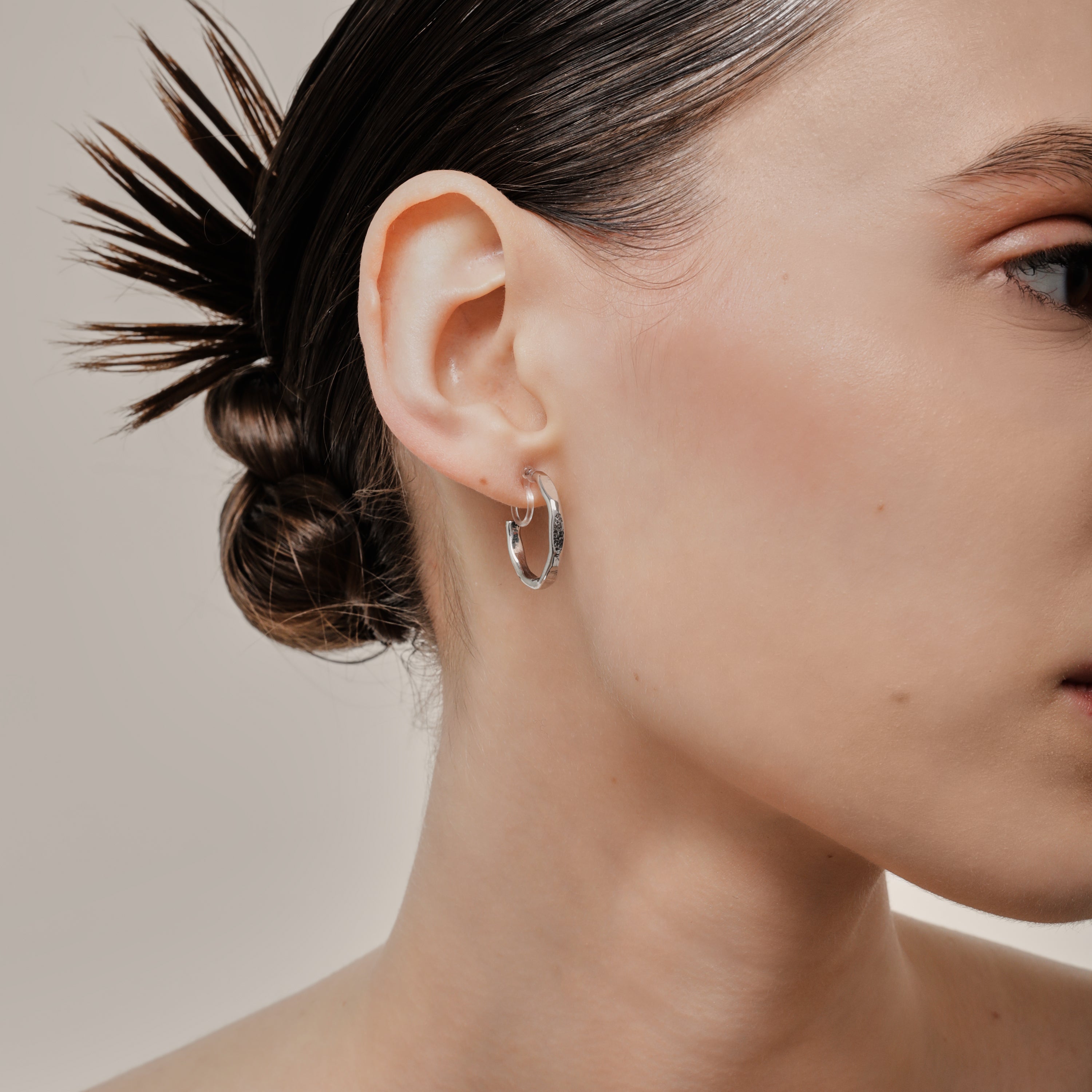 A model wearing the Smith Hoop Clip On Earrings in Silver, perfect for all ear sizes. With a resin clip-on closure and medium secure hold, these earrings provide comfort for 8-12 hours. Whether you have thick, large, or sensitive ears, these earrings are a must-have! Note: No adjustments possible and one pair only.