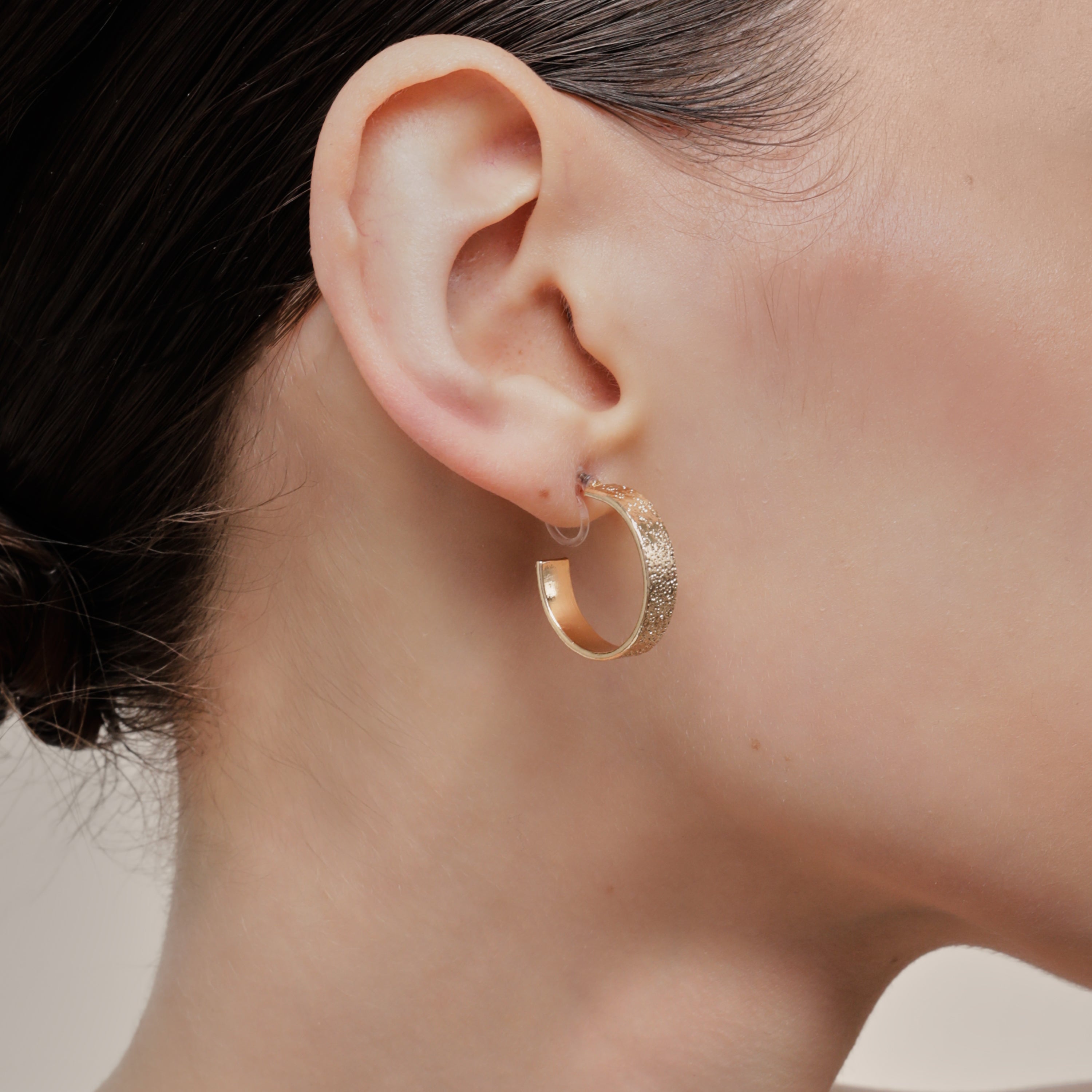 A model wearing the Speckled Hoop Clip On Earrings in Gold offer versatility and comfort for a range of ear sizes and sensitivities. With a medium secure hold, you can confidently wear them for 8-12 hours. Sold as a pair.