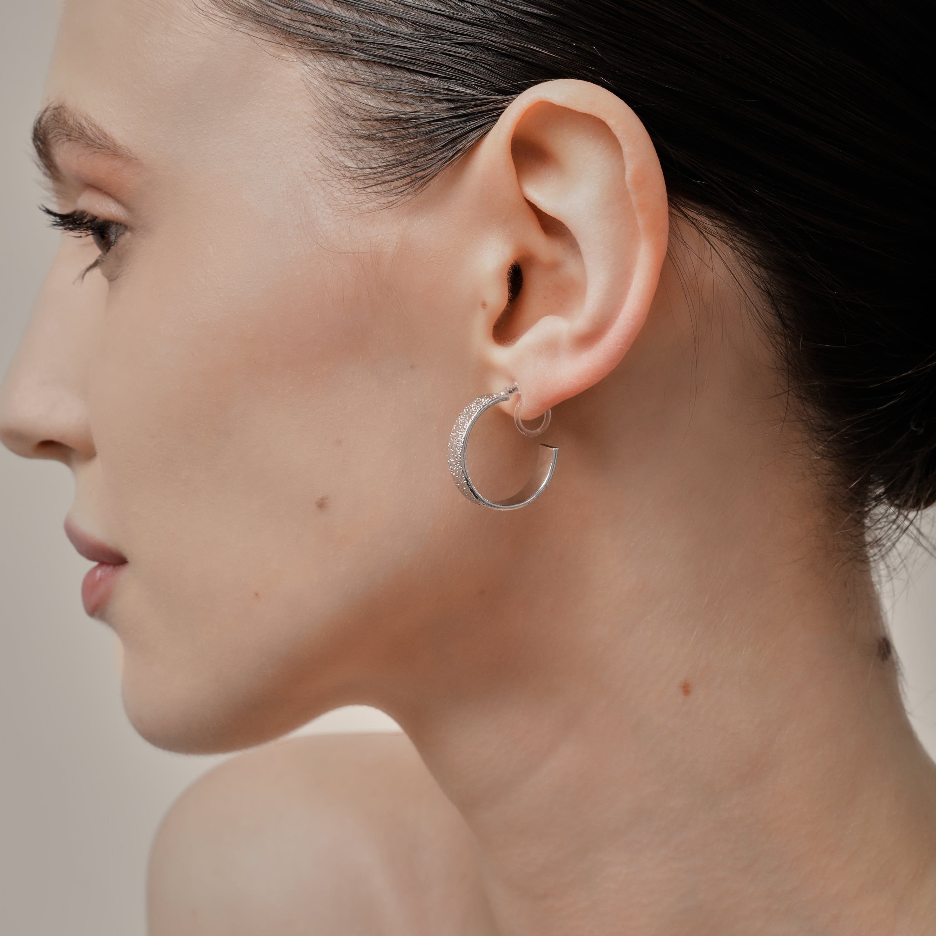A model wearing the Speckled Hoop Clip On Earrings in Silver offer versatility and comfort for a range of ear sizes and sensitivities. With a medium secure hold, you can confidently wear them for 8-12 hours. Sold as a pair.