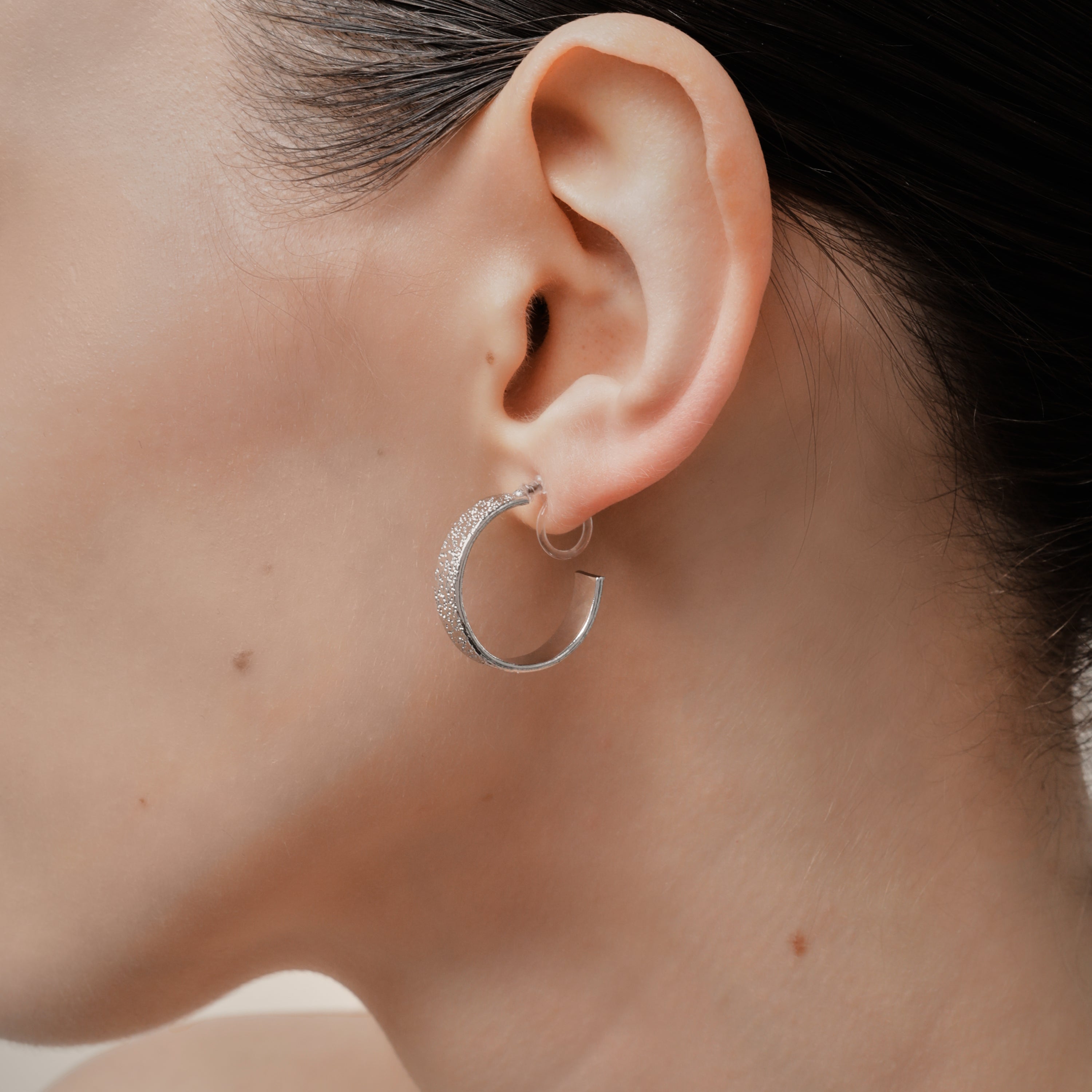 A model wearing the Speckled Hoop Clip On Earrings in Silver offer versatility and comfort for a range of ear sizes and sensitivities. With a medium secure hold, you can confidently wear them for 8-12 hours. Sold as a pair.