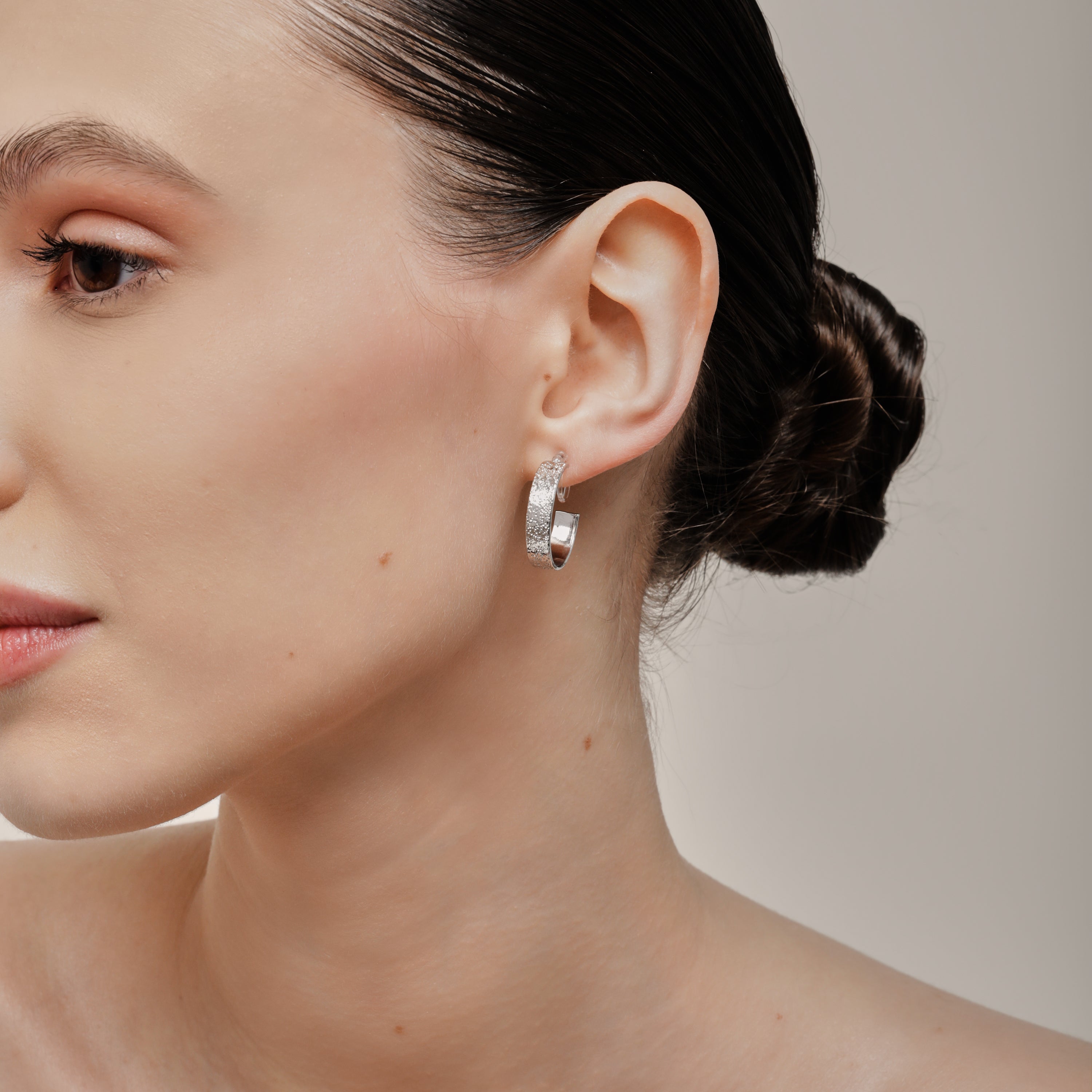 A model wearing the Speckled Hoop Clip On Earrings in Silver offer versatility and comfort for a range of ear sizes and sensitivities. With a medium secure hold, you can confidently wear them for 8-12 hours. Sold as a pair.