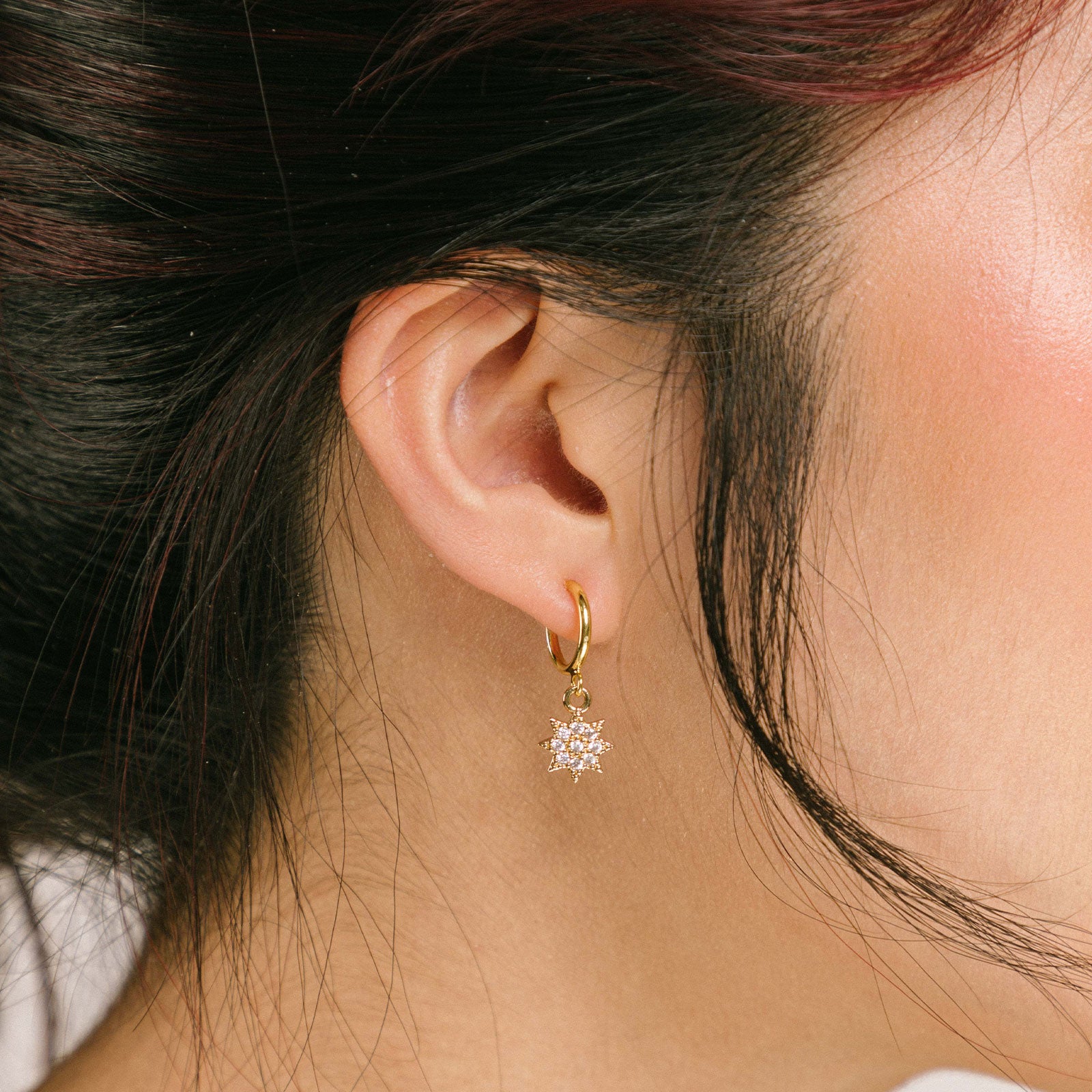 A model wearing the Star Charm Clip On Earring is designed with a sliding spring mechanism, ideal for those with smaller or thinner ear lobes. You can rely on a secure hold that can adjust to your ear thickness. Wear these earrings comfortably for 2 - 4 hours. Crafted from brass and cubic zirconia, this earring is sold as a single pair.