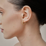 A model wearing the Sydney Pave Clip On Earrings in Gold for those with thick, sensitive, small, stretched, or keloid prone ears. Its medium secure hold and adjustable padding make it a comfortable and stylish choice. Made with high-quality gold tone copper alloy.