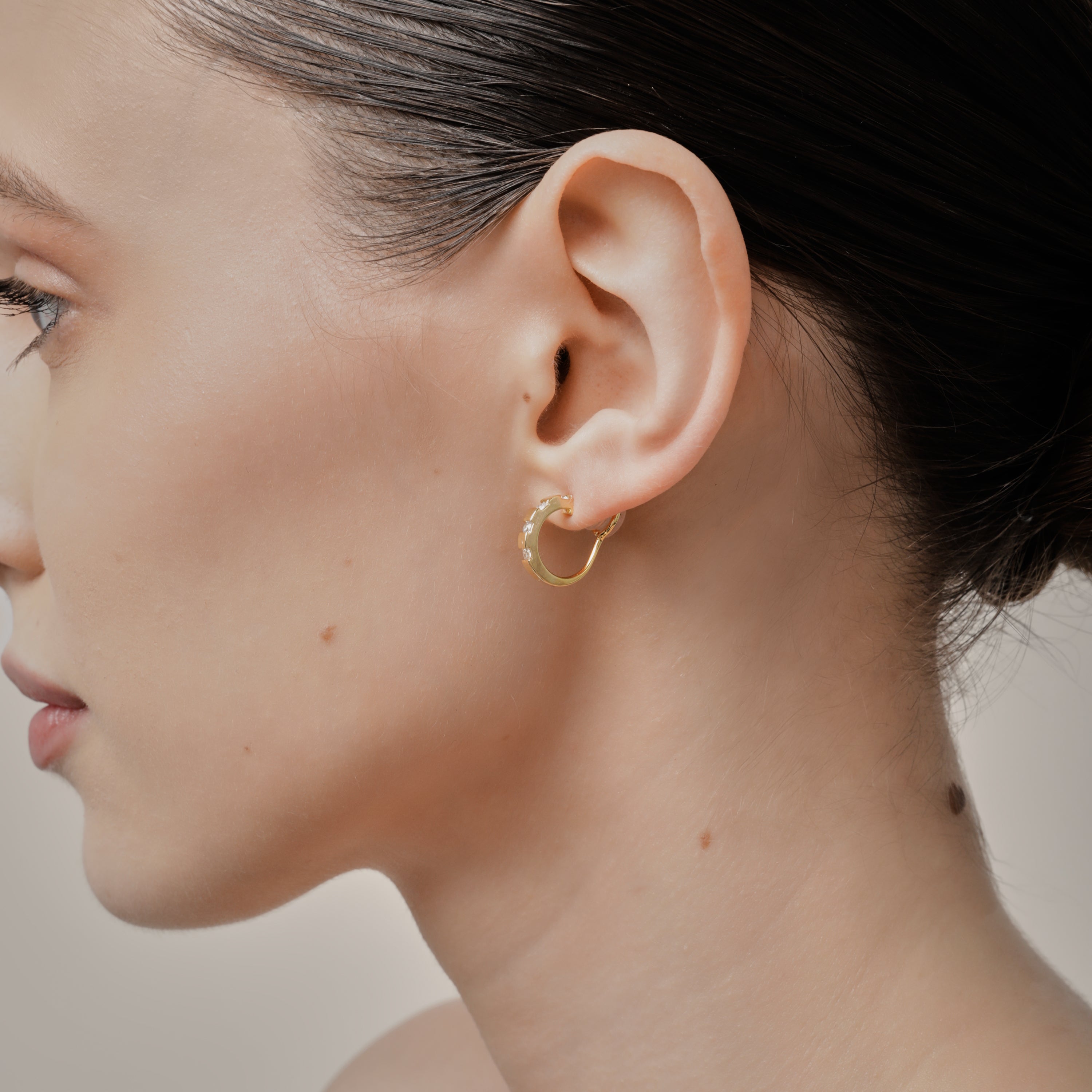 A model wearing the Sydney Pave Clip On Earrings in Gold for those with thick, sensitive, small, stretched, or keloid prone ears. Its medium secure hold and adjustable padding make it a comfortable and stylish choice. Made with high-quality gold tone copper alloy.