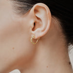 A model wearing the Sydney Pave Clip On Earrings in Gold for those with thick, sensitive, small, stretched, or keloid prone ears. Its medium secure hold and adjustable padding make it a comfortable and stylish choice. Made with high-quality gold tone copper alloy.
