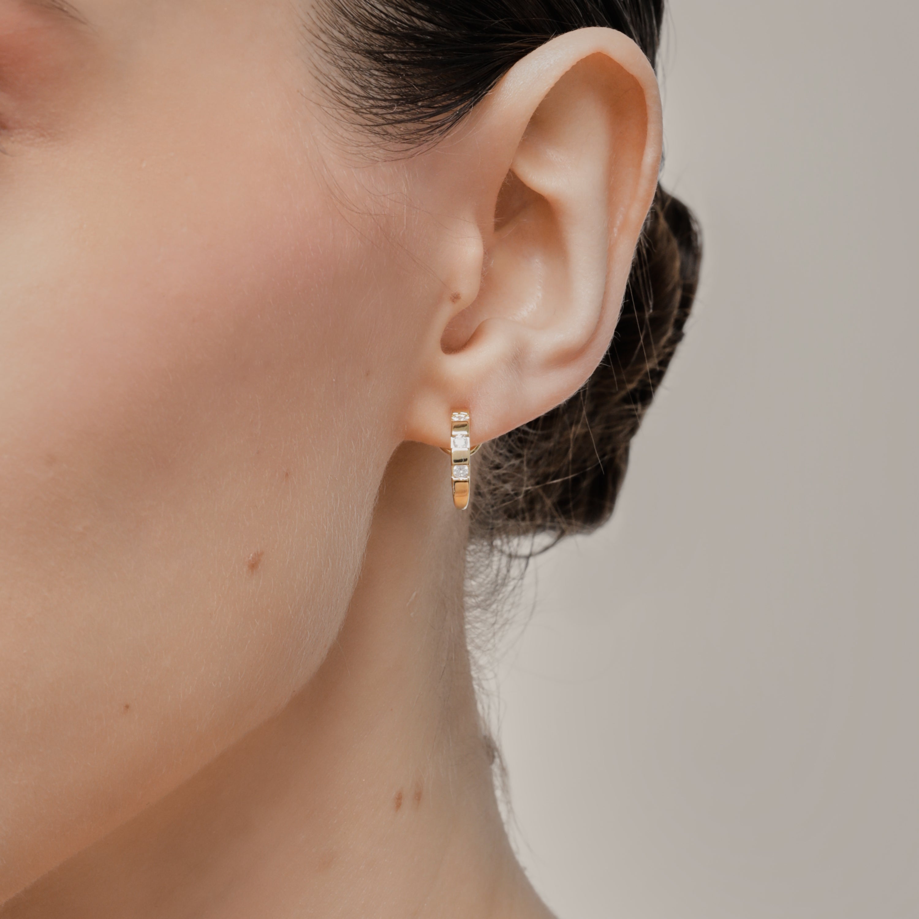 A model wearing the Sydney Pave Clip On Earrings in Gold for those with thick, sensitive, small, stretched, or keloid prone ears. Its medium secure hold and adjustable padding make it a comfortable and stylish choice. Made with high-quality gold tone copper alloy.