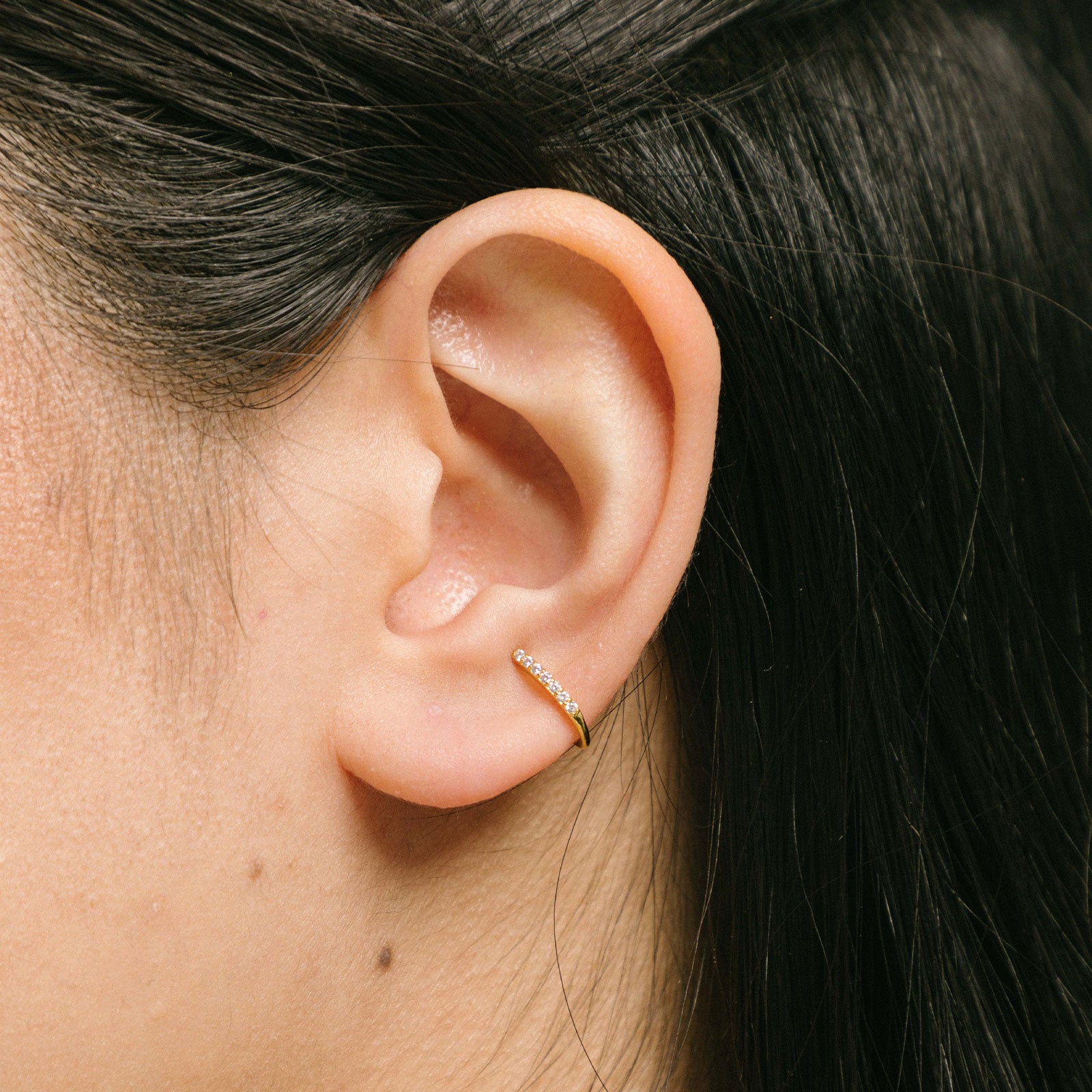 A model wearing the Thin Band Ear Cuff offers Medium Secure hold for up to 24 hours of comfortable wear. This ear cuff can be adjusted slightly once on the ear, and is ideal for all ear types, including thick/large ears, sensitive ears, small/thin ears, and stretched/healing ears. It is crafted from gold or silver plated copper alloy, with Cubic Zirconia for sparkle. This one-piece ear cuff also doubles as a faux nose piercing.
