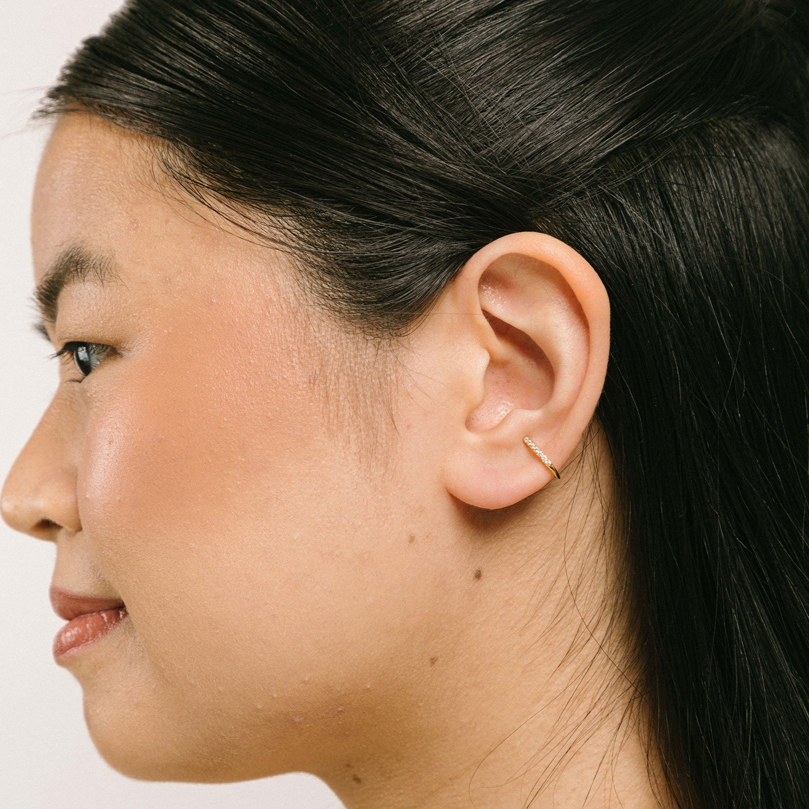 A model wearing the Thin Band Ear Cuff offers Medium Secure hold for up to 24 hours of comfortable wear. This ear cuff can be adjusted slightly once on the ear, and is ideal for all ear types, including thick/large ears, sensitive ears, small/thin ears, and stretched/healing ears. It is crafted from gold or silver plated copper alloy, with Cubic Zirconia for sparkle. This one-piece ear cuff also doubles as a faux nose piercing.