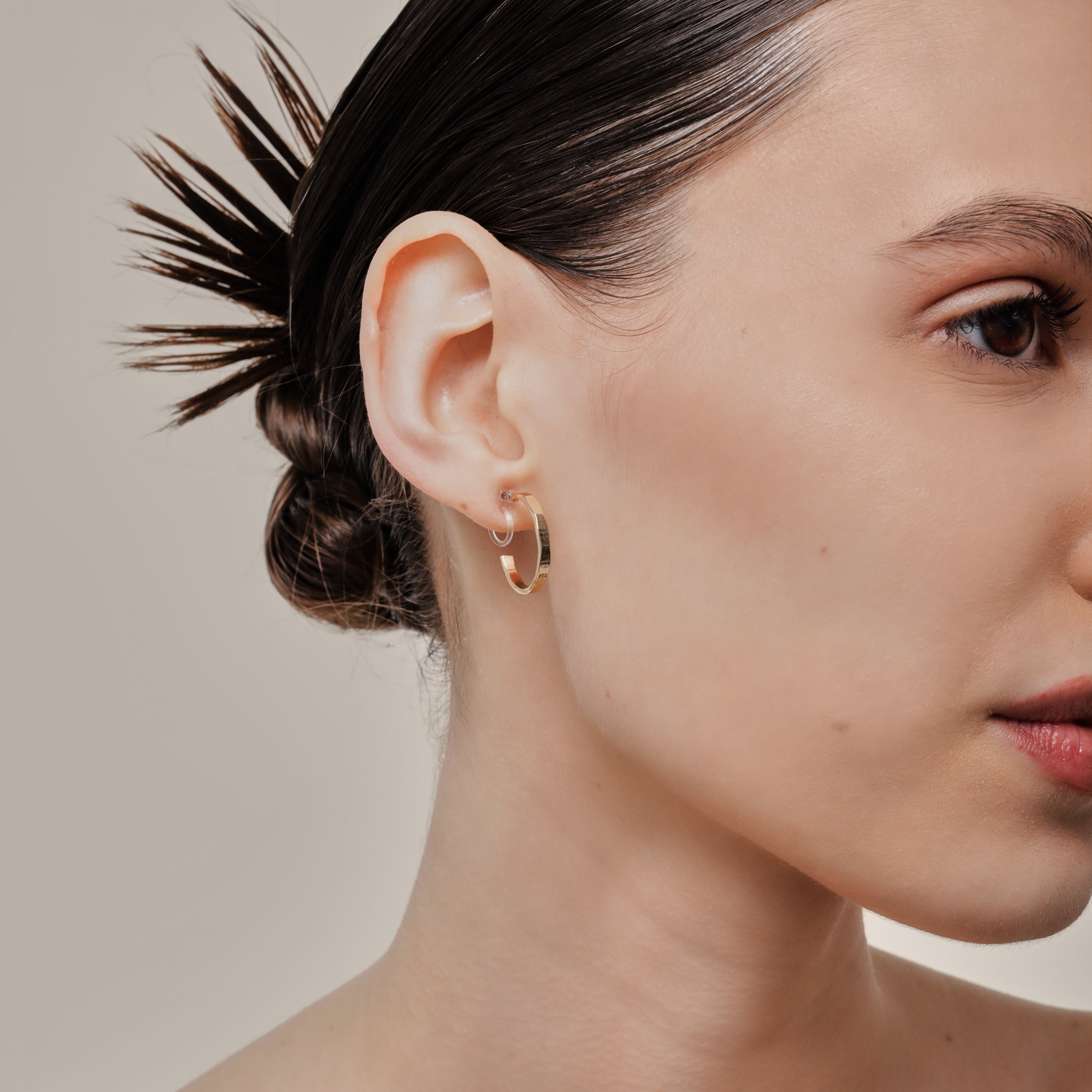A model wearing the Tia Hoop Clip On Earrings in Gold are a must-have accessory. With a resin clip-on closure, they offer a secure hold for 8-12 hours of comfortable wear. Perfect for sensitive or small ears, and even those with thick or large ears. Please note, one pair included.