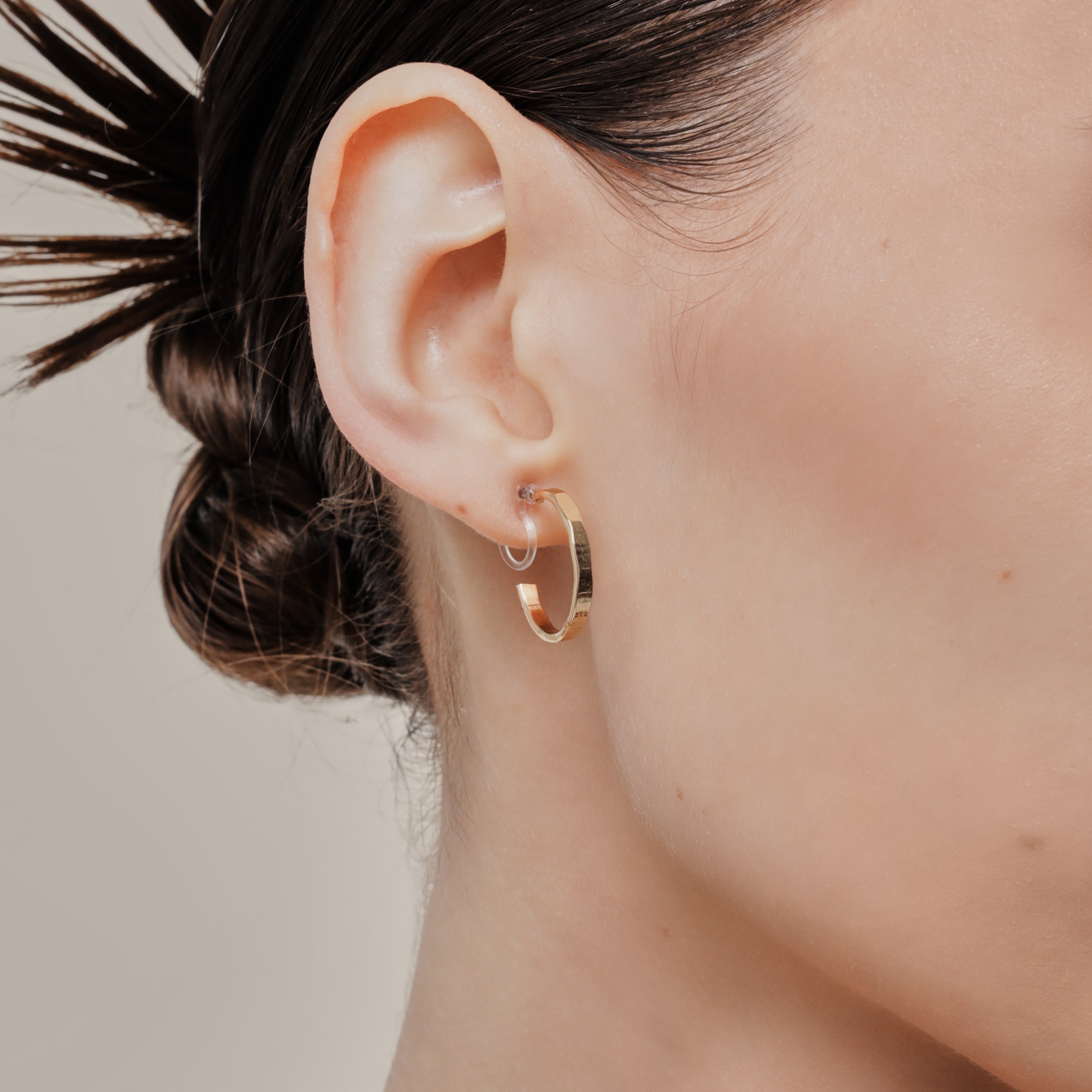 A model wearing the Tia Hoop Clip On Earrings in Gold are a must-have accessory. With a resin clip-on closure, they offer a secure hold for 8-12 hours of comfortable wear. Perfect for sensitive or small ears, and even those with thick or large ears. Please note, one pair included.