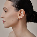 A model wearing the Tia Hoop Clip On Earrings in Silver are a must-have accessory. With a resin clip-on closure, they offer a secure hold for 8-12 hours of comfortable wear. Perfect for sensitive or small ears, and even those with thick or large ears. Please note, one pair included.