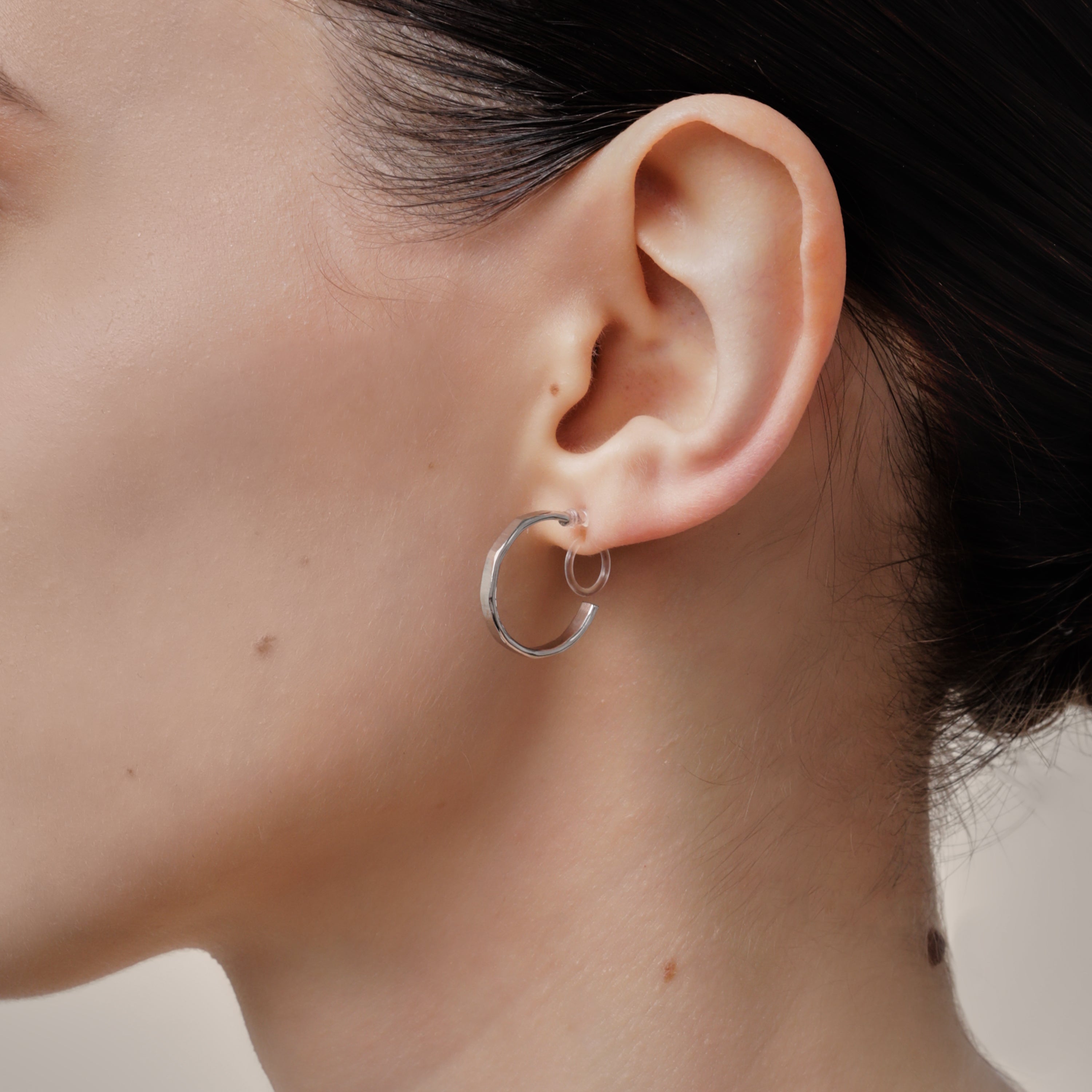 A model wearing the Tia Hoop Clip On Earrings in Silver are a must-have accessory. With a resin clip-on closure, they offer a secure hold for 8-12 hours of comfortable wear. Perfect for sensitive or small ears, and even those with thick or large ears. Please note, one pair included.