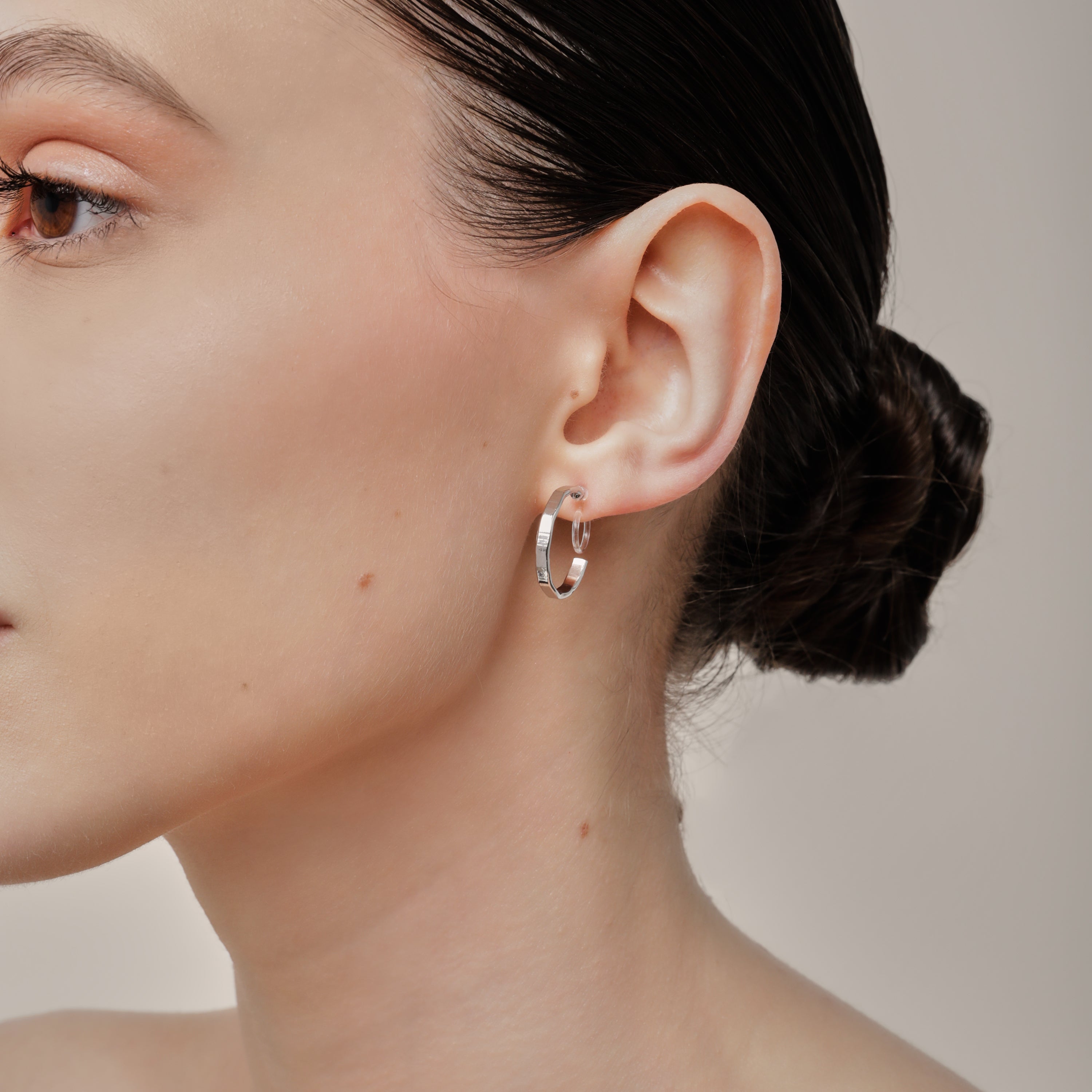 A model wearing the Tia Hoop Clip On Earrings in Silver are a must-have accessory. With a resin clip-on closure, they offer a secure hold for 8-12 hours of comfortable wear. Perfect for sensitive or small ears, and even those with thick or large ears. Please note, one pair included.