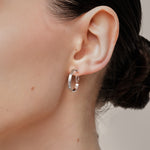 A model wearing the Tia Hoop Clip On Earrings in Silver are a must-have accessory. With a resin clip-on closure, they offer a secure hold for 8-12 hours of comfortable wear. Perfect for sensitive or small ears, and even those with thick or large ears. Please note, one pair included.