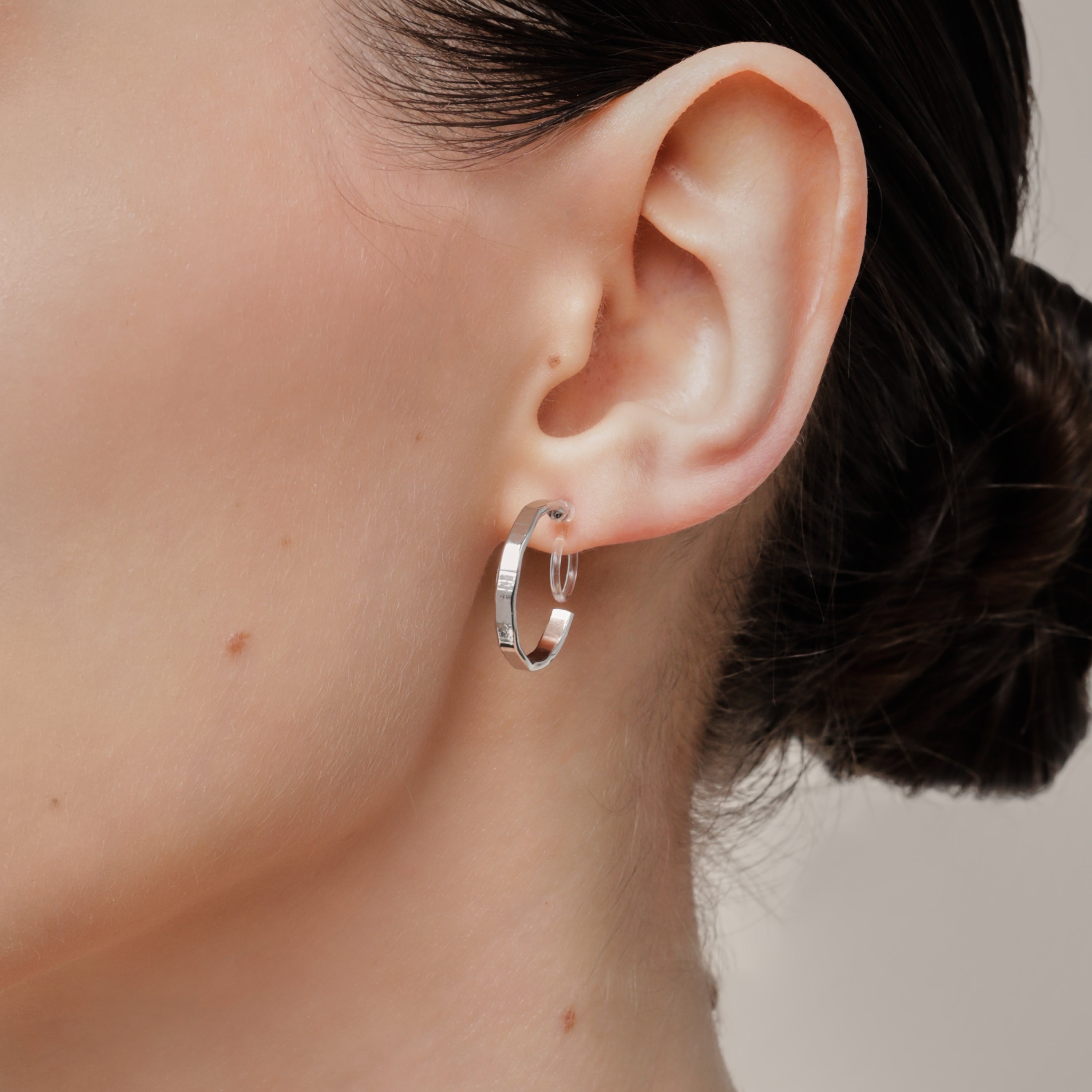 A model wearing the Tia Hoop Clip On Earrings in Silver are a must-have accessory. With a resin clip-on closure, they offer a secure hold for 8-12 hours of comfortable wear. Perfect for sensitive or small ears, and even those with thick or large ears. Please note, one pair included.