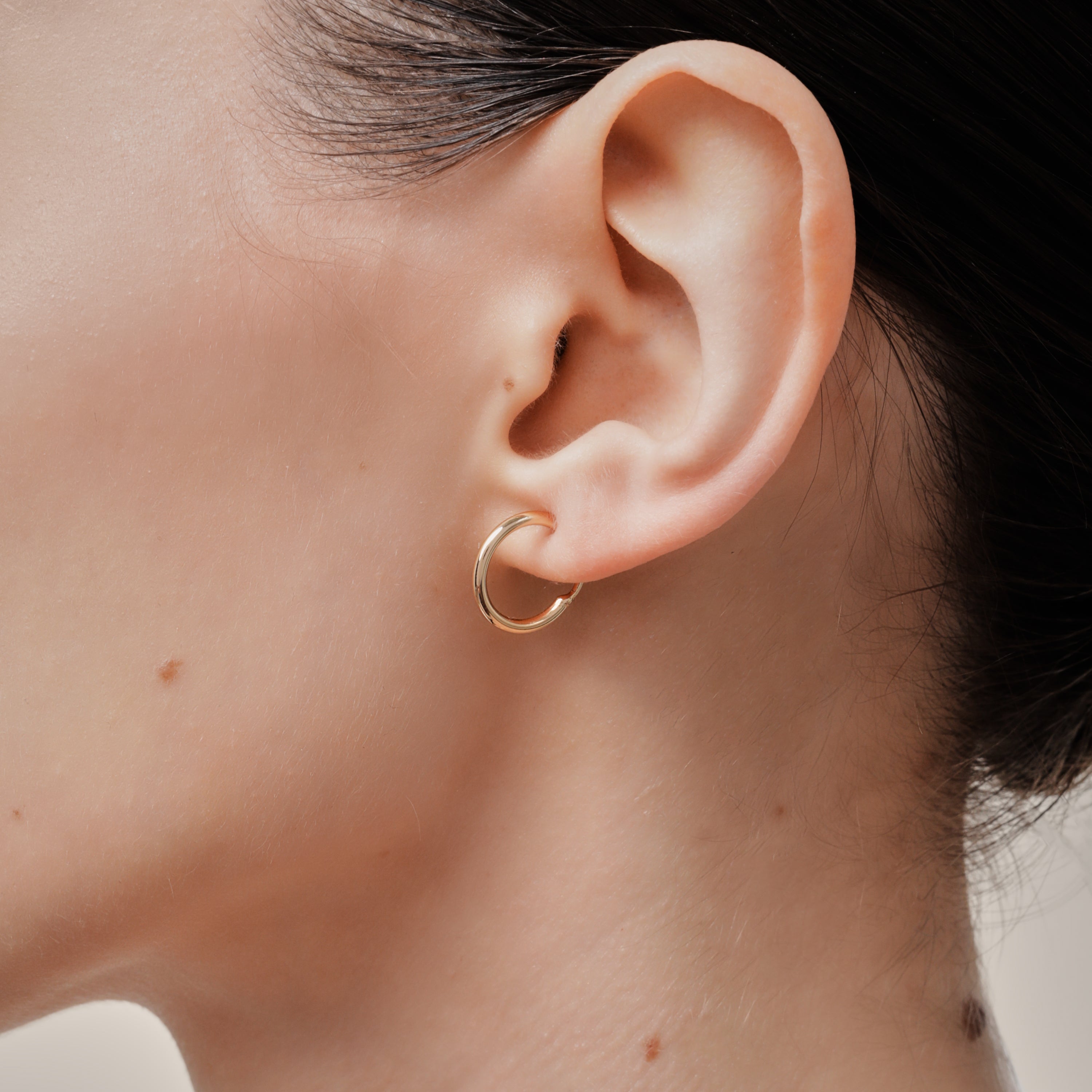 A model wearing the Tiny Hoop Clip On Earrings in Gold offer a Mosquito Coil Clip-On Closure, designed for comfort and versatility. Perfect for various ear types, they provide a secure hold and comfortable wear for 24 hours.