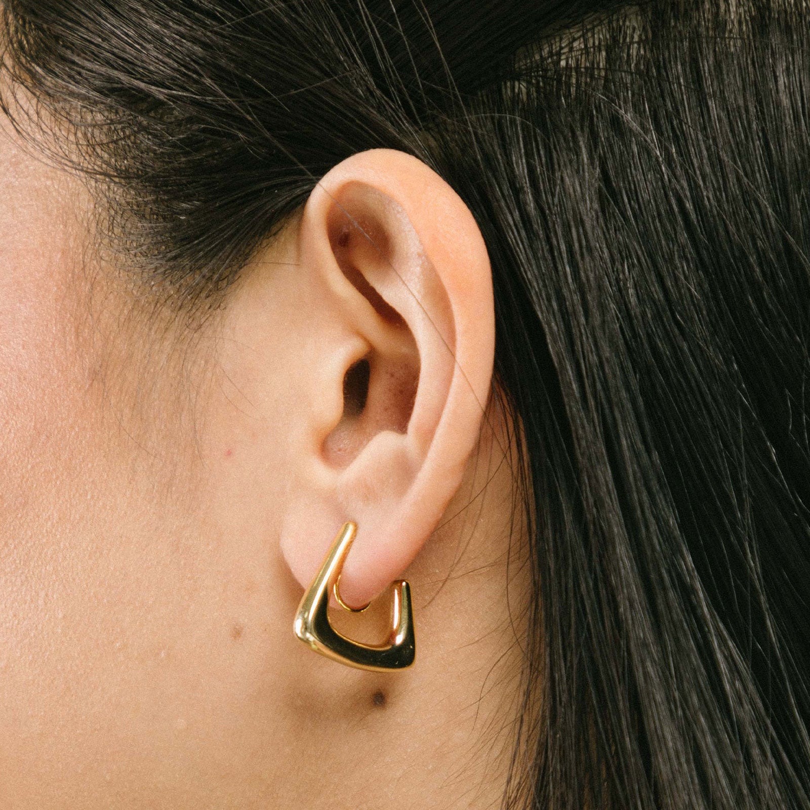 A model wearing our Triangle Hoop Clip-On Earrings - 18k gold-plated metal alloy, non-tarnish, and water-resistant. Modern clip-on with mosquito coil closure for secure wear. Classic triangle hoop shape for a stylish look, perfect for everyday wear.