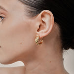 A model wearing the Trinity Hoop Clip On Earrings in Gold are perfect for those with various ear types, including thick, sensitive, small, stretched, and keloid-prone ears. Featuring a Mosquito Coil Clip-On Closure, they provide a secure hold for up to 24 hours of comfortable wear. With easily adjustable padding, these earrings are suitable for all-day wear. Please note that this item includes only one pair.