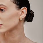 A model wearing the Trinity Hoop Clip On Earrings in Gold are perfect for those with various ear types, including thick, sensitive, small, stretched, and keloid-prone ears. Featuring a Mosquito Coil Clip-On Closure, they provide a secure hold for up to 24 hours of comfortable wear. With easily adjustable padding, these earrings are suitable for all-day wear. Please note that this item includes only one pair.
