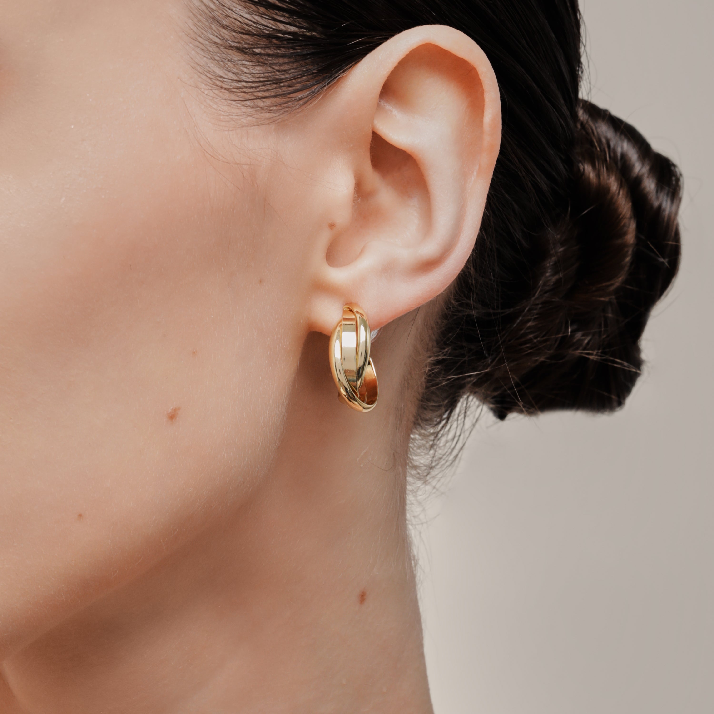 A model wearing the Trinity Hoop Clip On Earrings in Gold are perfect for those with various ear types, including thick, sensitive, small, stretched, and keloid-prone ears. Featuring a Mosquito Coil Clip-On Closure, they provide a secure hold for up to 24 hours of comfortable wear. With easily adjustable padding, these earrings are suitable for all-day wear. Please note that this item includes only one pair.