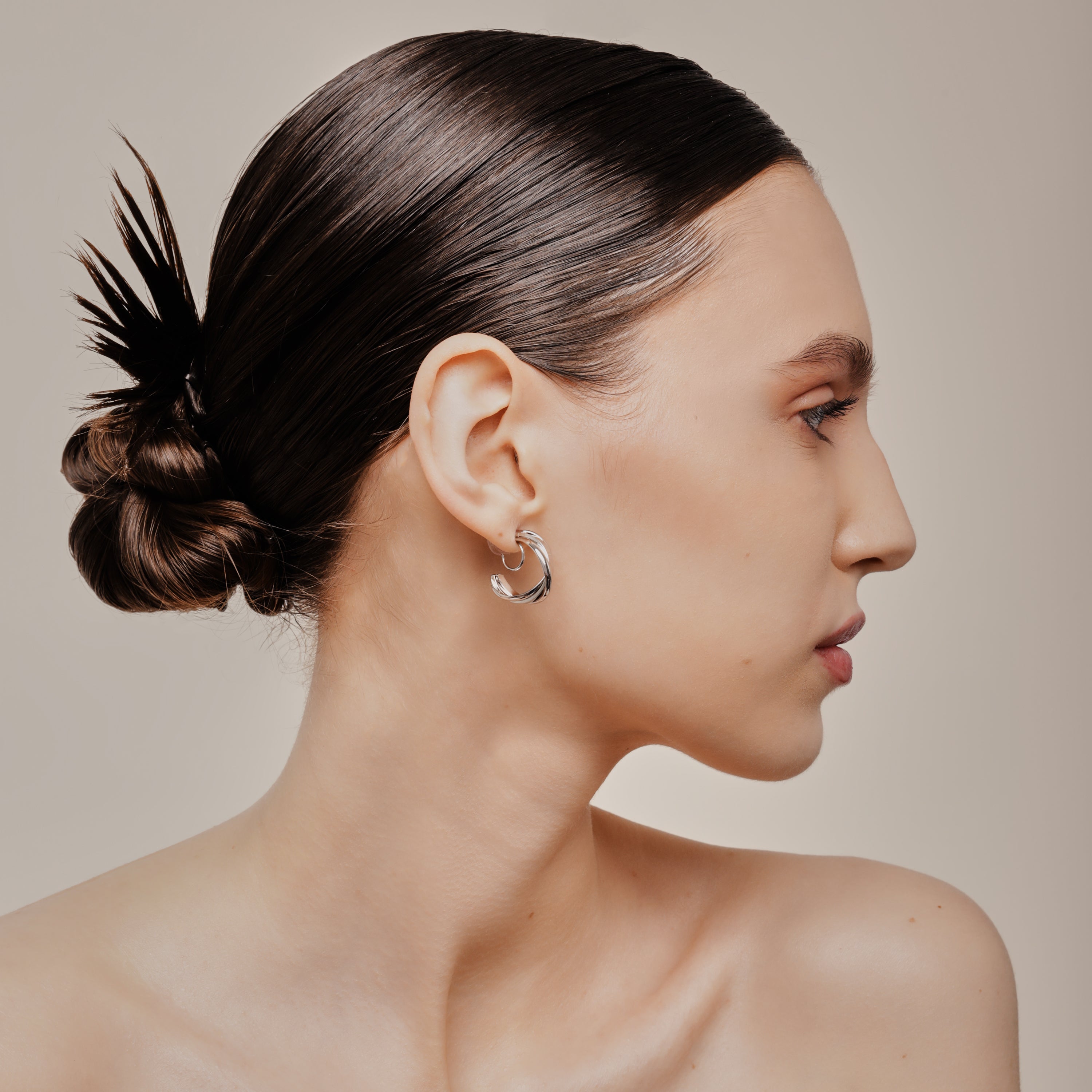A model wearing the Trinity Hoop Clip On Earrings in Silver are perfect for those with various ear types, including thick, sensitive, small, stretched, and keloid-prone ears. Featuring a Mosquito Coil Clip-On Closure, they provide a secure hold for up to 24 hours of comfortable wear. With easily adjustable padding, these earrings are suitable for all-day wear. Please note that this item includes only one pair.