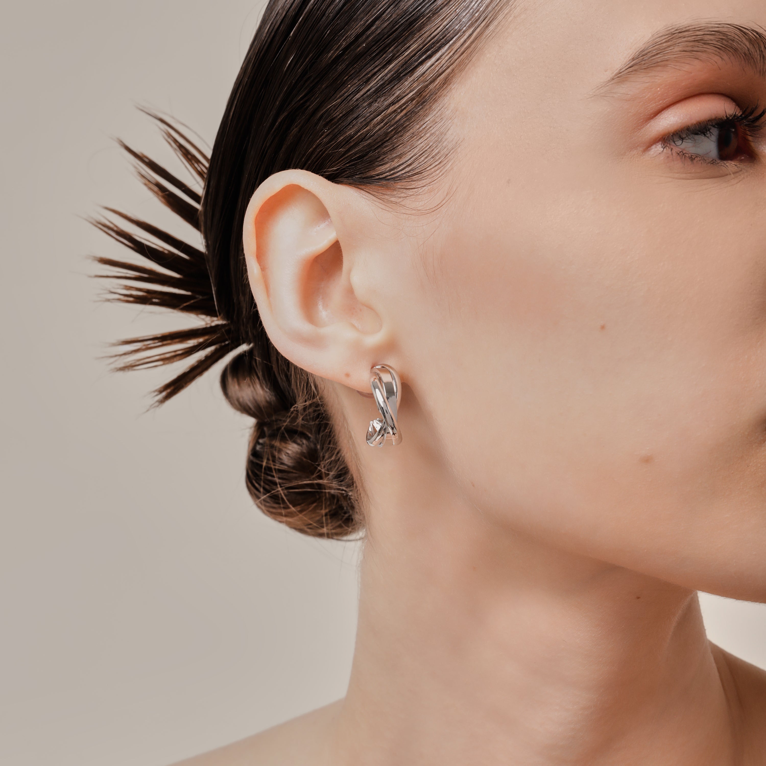 A model wearing the Trinity Hoop Clip On Earrings in Silver are perfect for those with various ear types, including thick, sensitive, small, stretched, and keloid-prone ears. Featuring a Mosquito Coil Clip-On Closure, they provide a secure hold for up to 24 hours of comfortable wear. With easily adjustable padding, these earrings are suitable for all-day wear. Please note that this item includes only one pair.