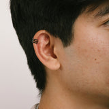 A model wearing the Triple Band Ear Cuff features a secure medium hold, adjustable fit, and non-tarnish, water-resistant stainless steel and titanium construction. Its 9mm diameter and 6mm width makes it ideal for all ear types, including thick/large, sensitive, small/thin, and stretched/healing ears. Average comfortable wear duration is up to 24 hours for one piece. Intended to be worn on the helix of the ear.